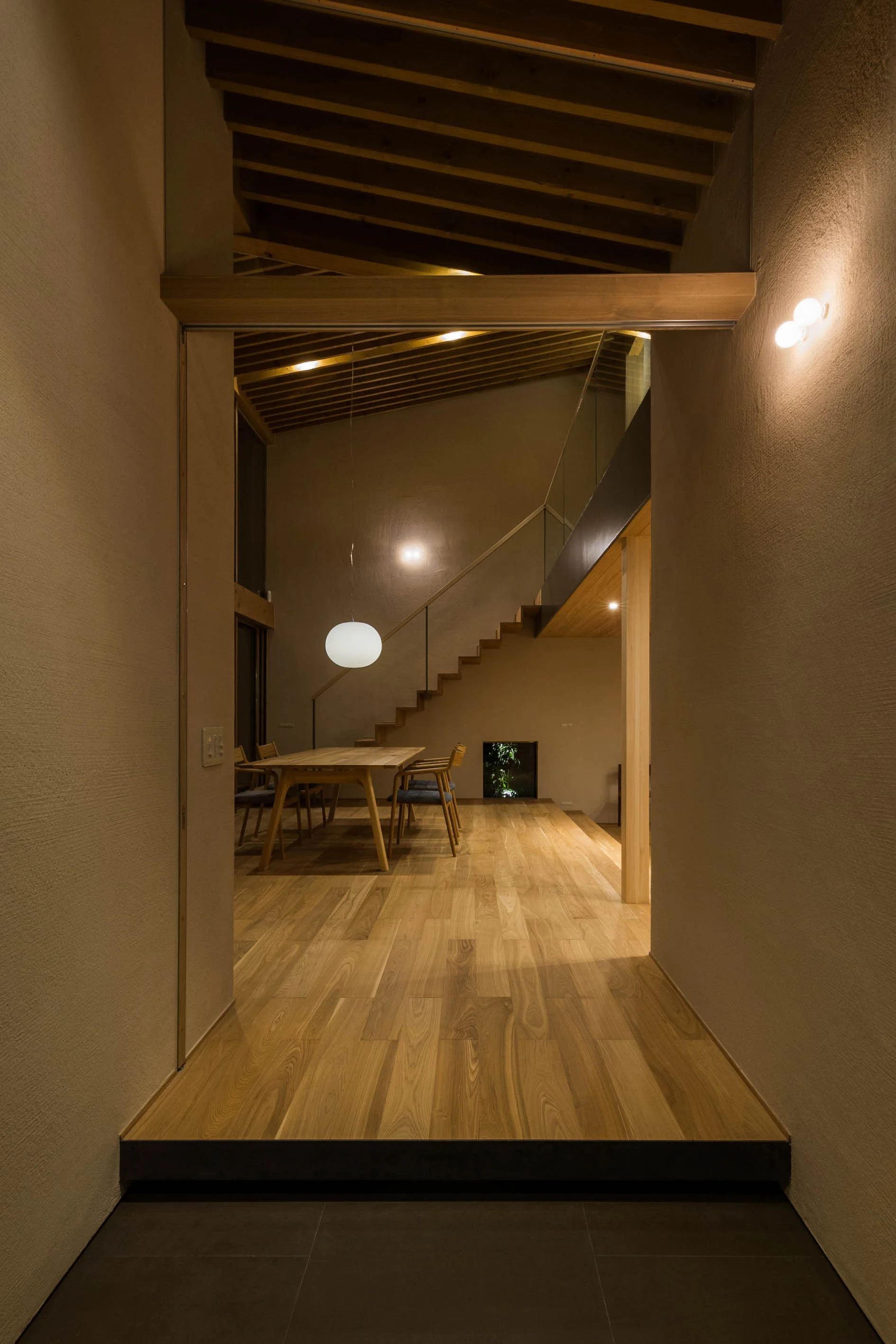 A dining room with a wooden table, chairs, and a globe pendant light sits on a raised wood floor under an exposed timber ceiling.