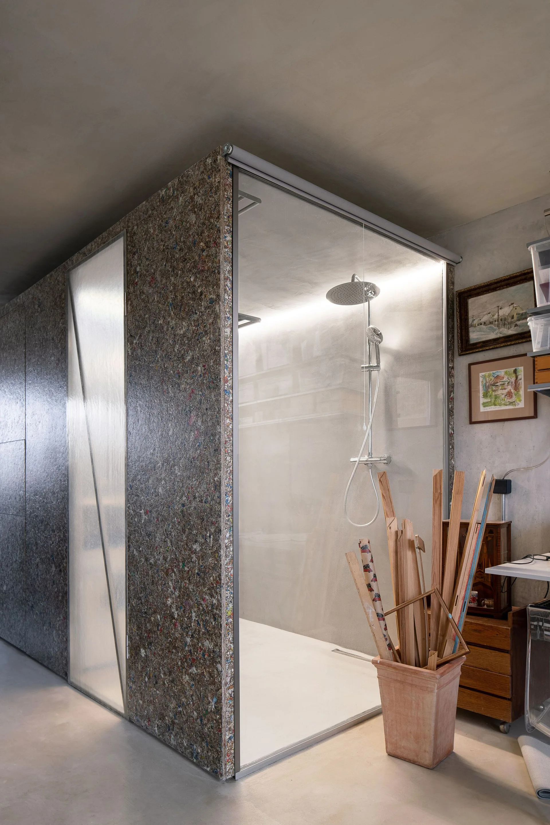 A modern walk-in shower cabin with clear glass, a textured glass door, speckled recycled composite cladding, and concrete-finish walls.