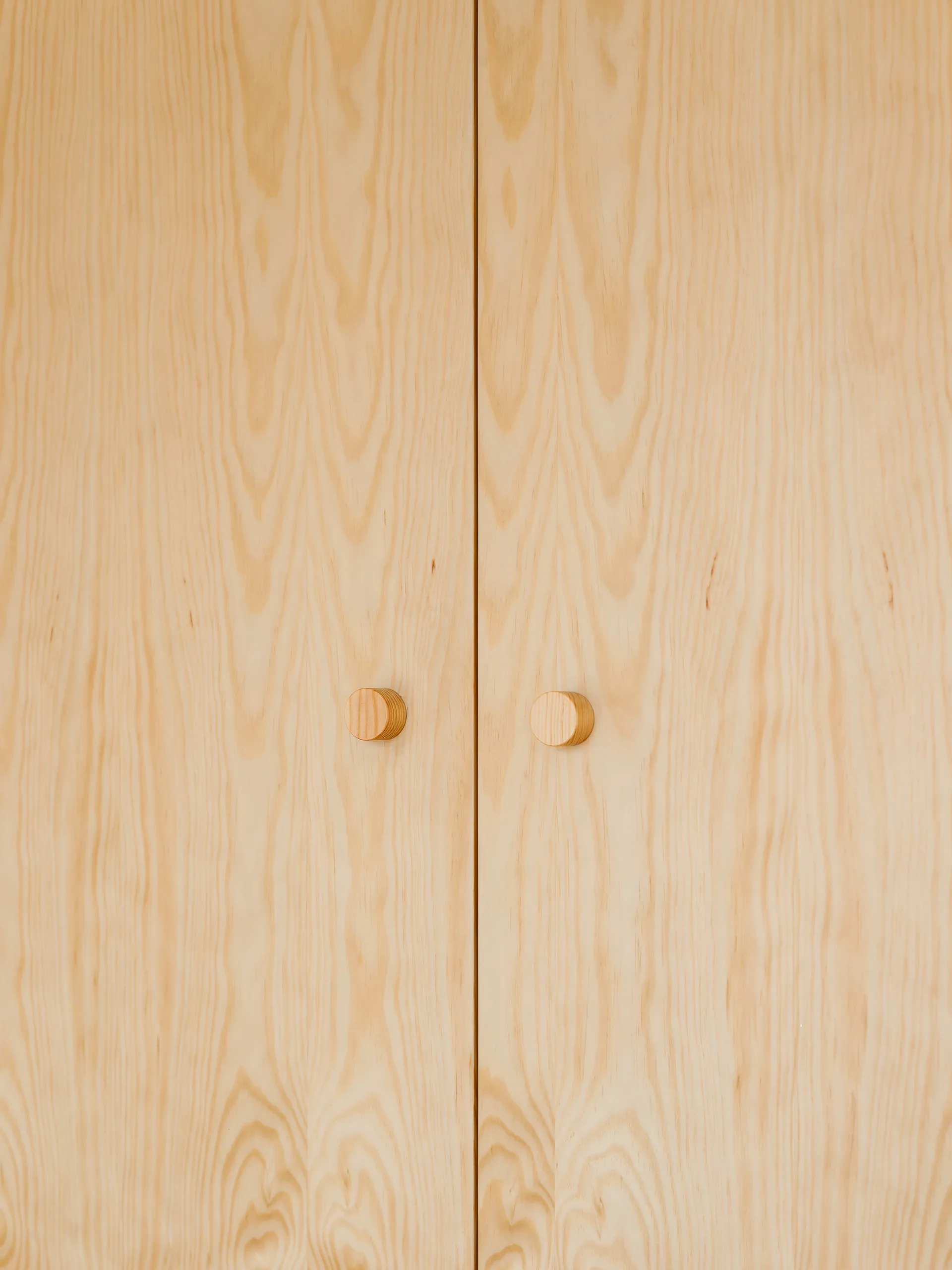 Two light wood cabinet doors with a prominent natural grain pattern and small cylindrical wooden knobs.