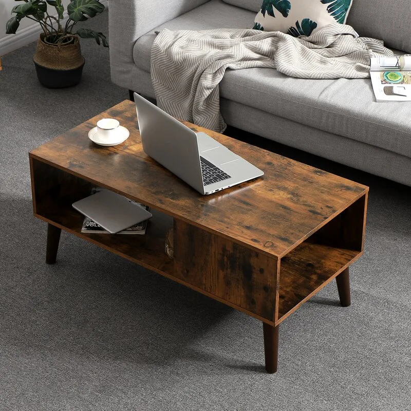 A rectangular distressed wood coffee table with tapered legs and a lower storage shelf sits on a gray carpet next to a gray sofa.