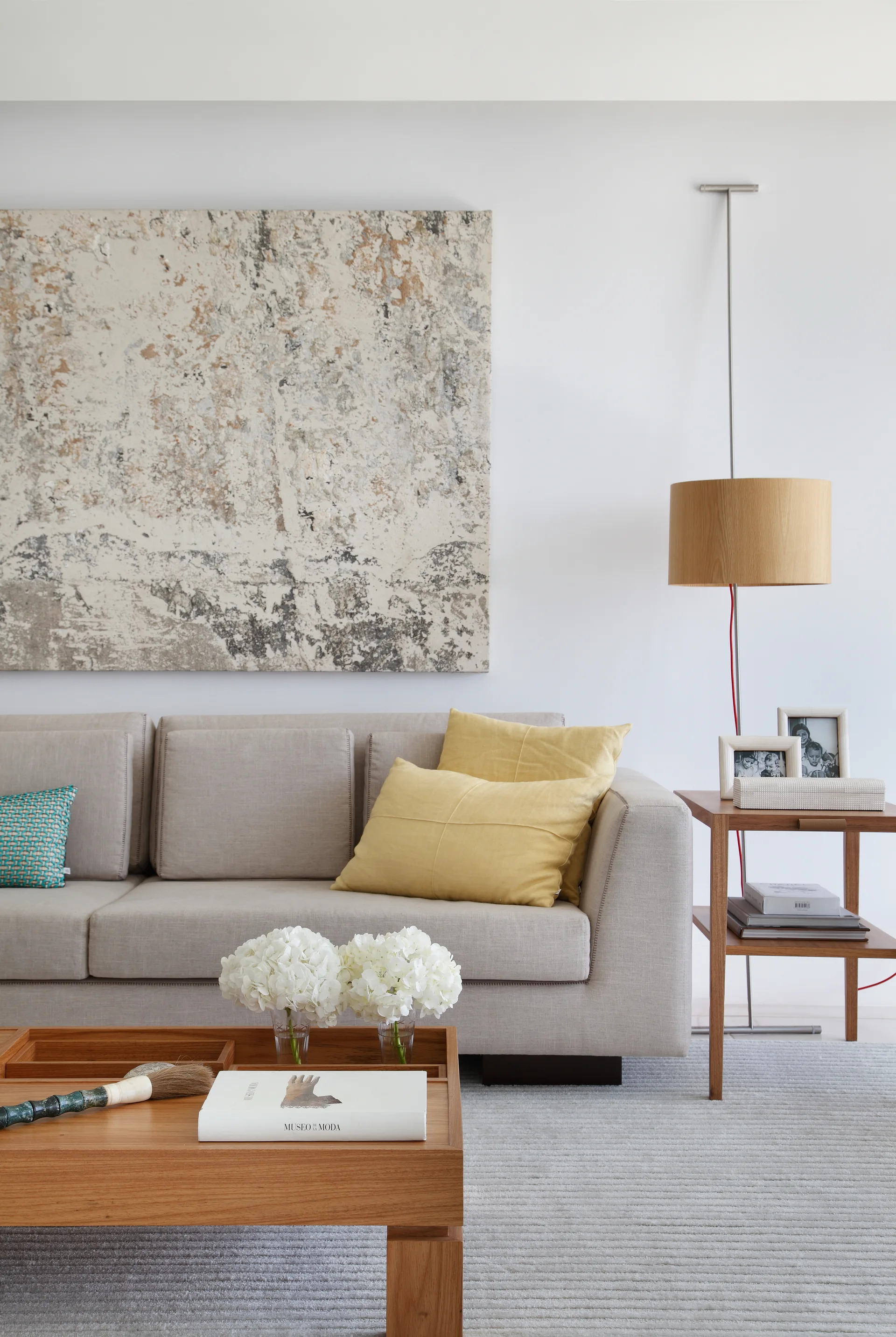 A beige sofa sits beneath a large abstract canvas painting, accompanied by a wooden coffee table and a wood-shaded floor lamp.