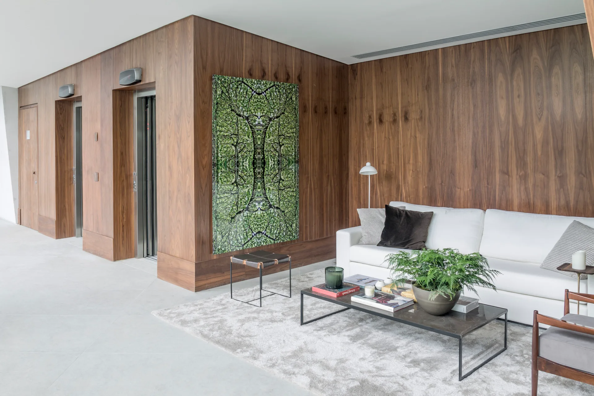 A modern lobby lounge features a white fabric sofa, a dark low coffee table, and a large green artwork against rich walnut-paneled walls.