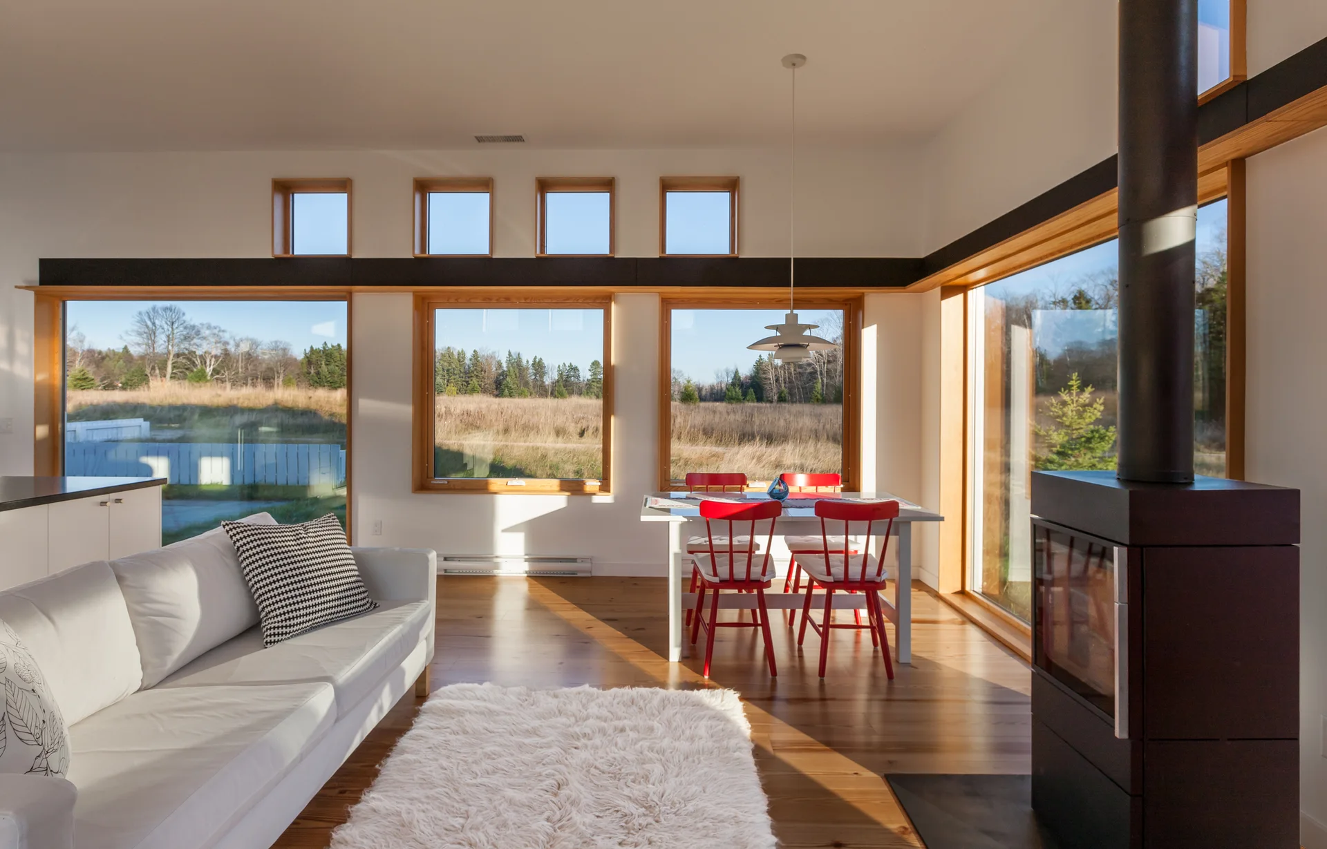 An open living and dining area with a white sofa, a black wood stove, and a white dining table surrounded by red chairs.