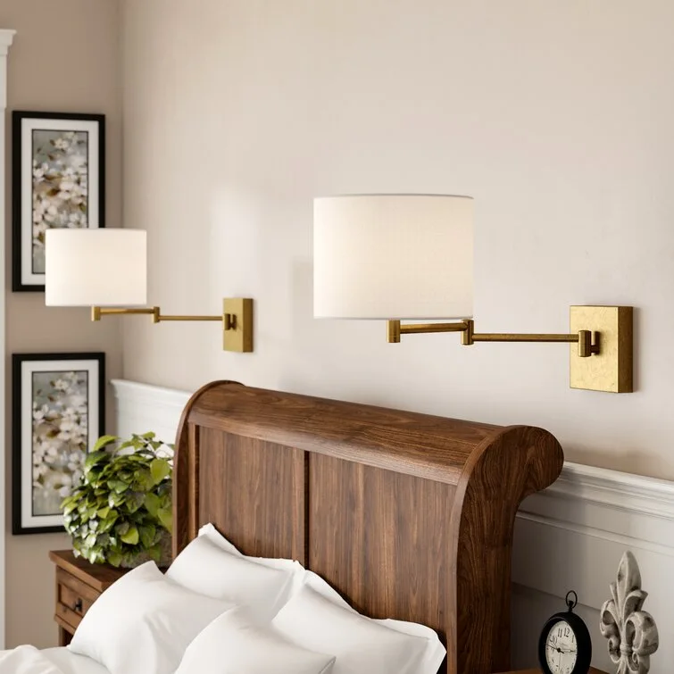 A traditional wooden headboard in a bedroom is flanked by two brass swing-arm wall lamps with white drum shades.