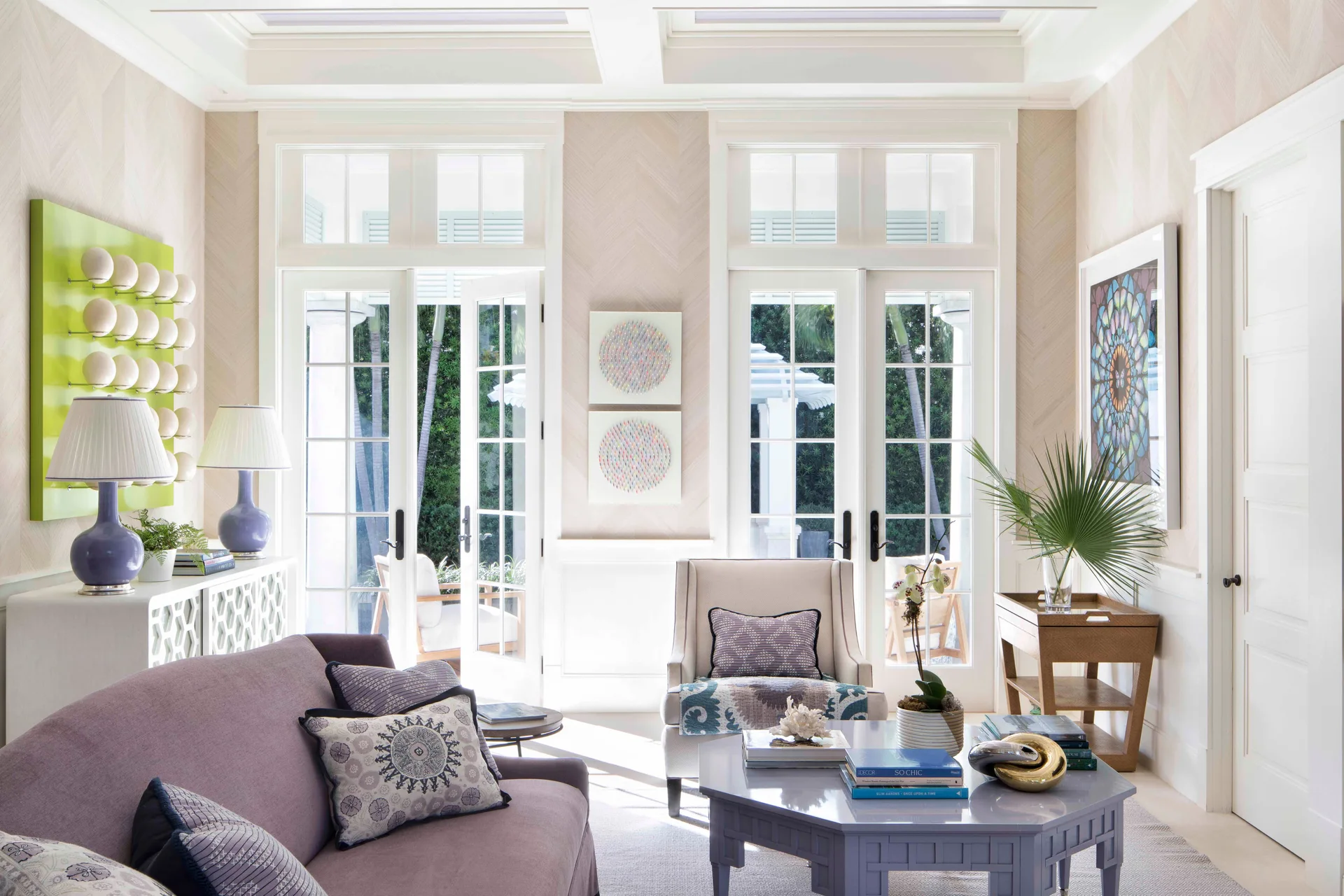 A bright living room features a lavender sofa, a hexagonal coffee table, chevron wallpaper, and french doors opening to the outdoors.
