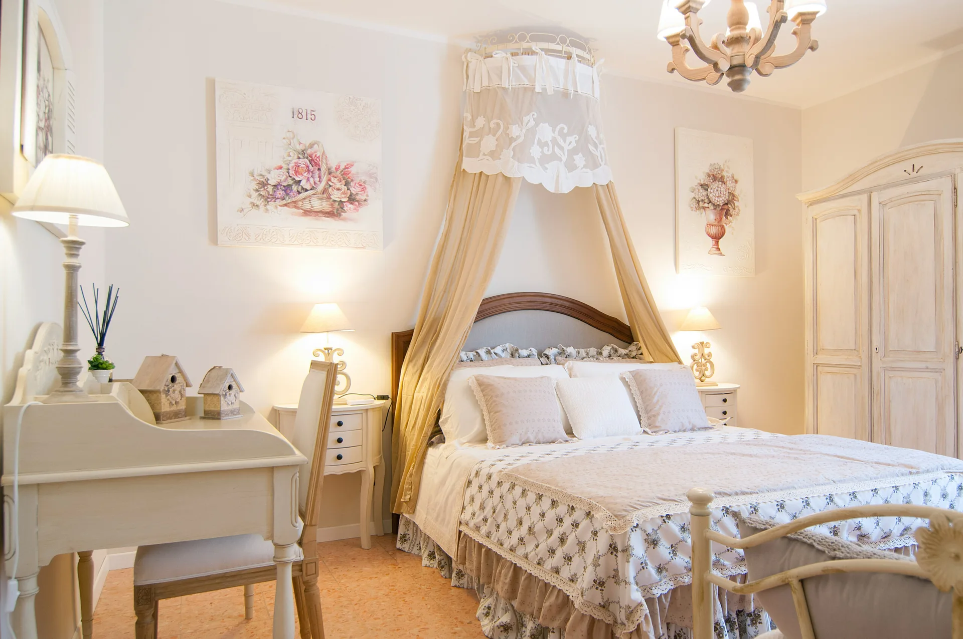 A shabby chic bedroom features a canopy bed with beige drapes, distressed wood furniture, a writing desk, and warm bedside lamps.