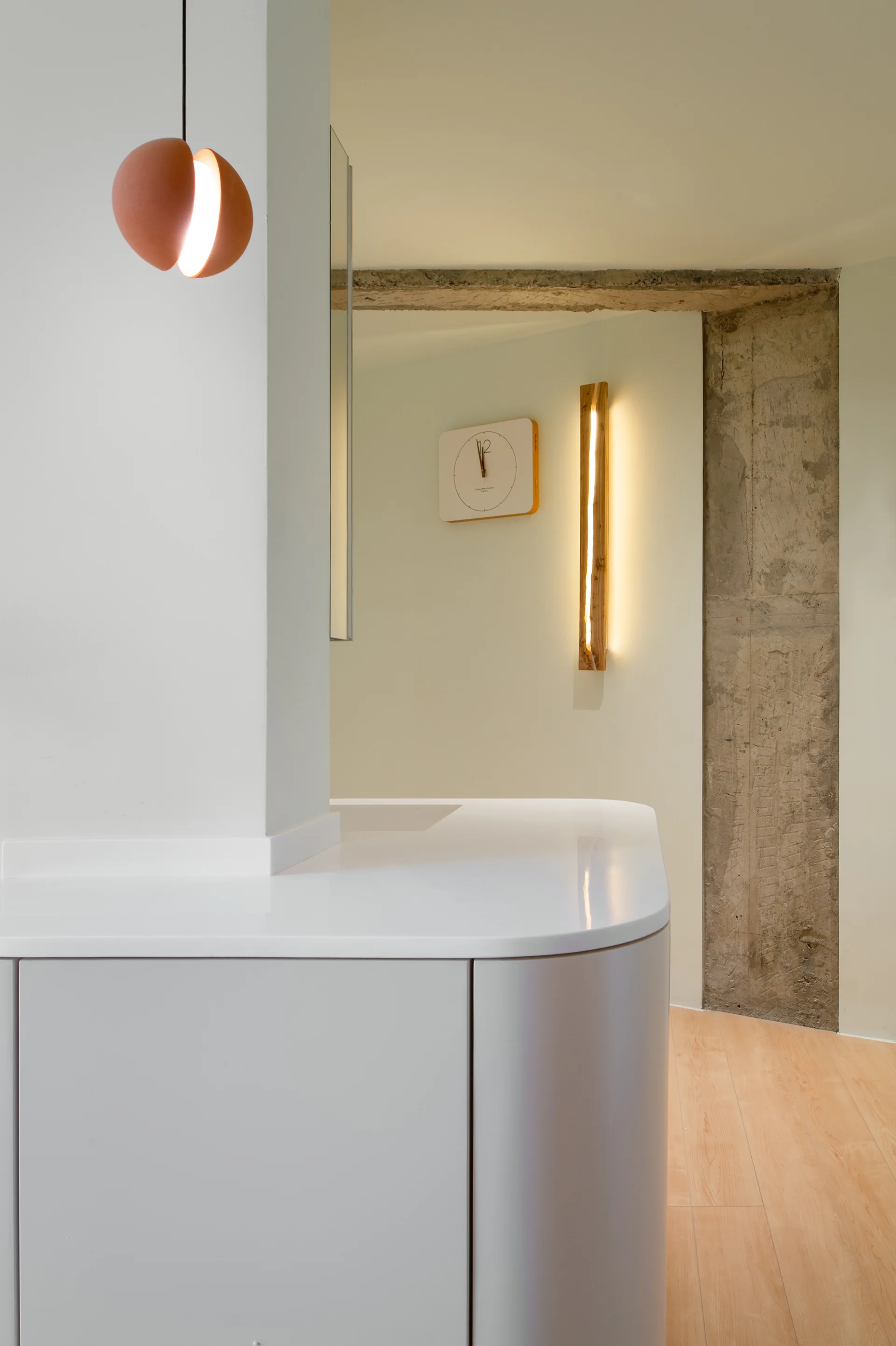 A minimalist interior featuring a curved white cabinet base, an exposed raw concrete column, and a modern terracotta pendant light.
