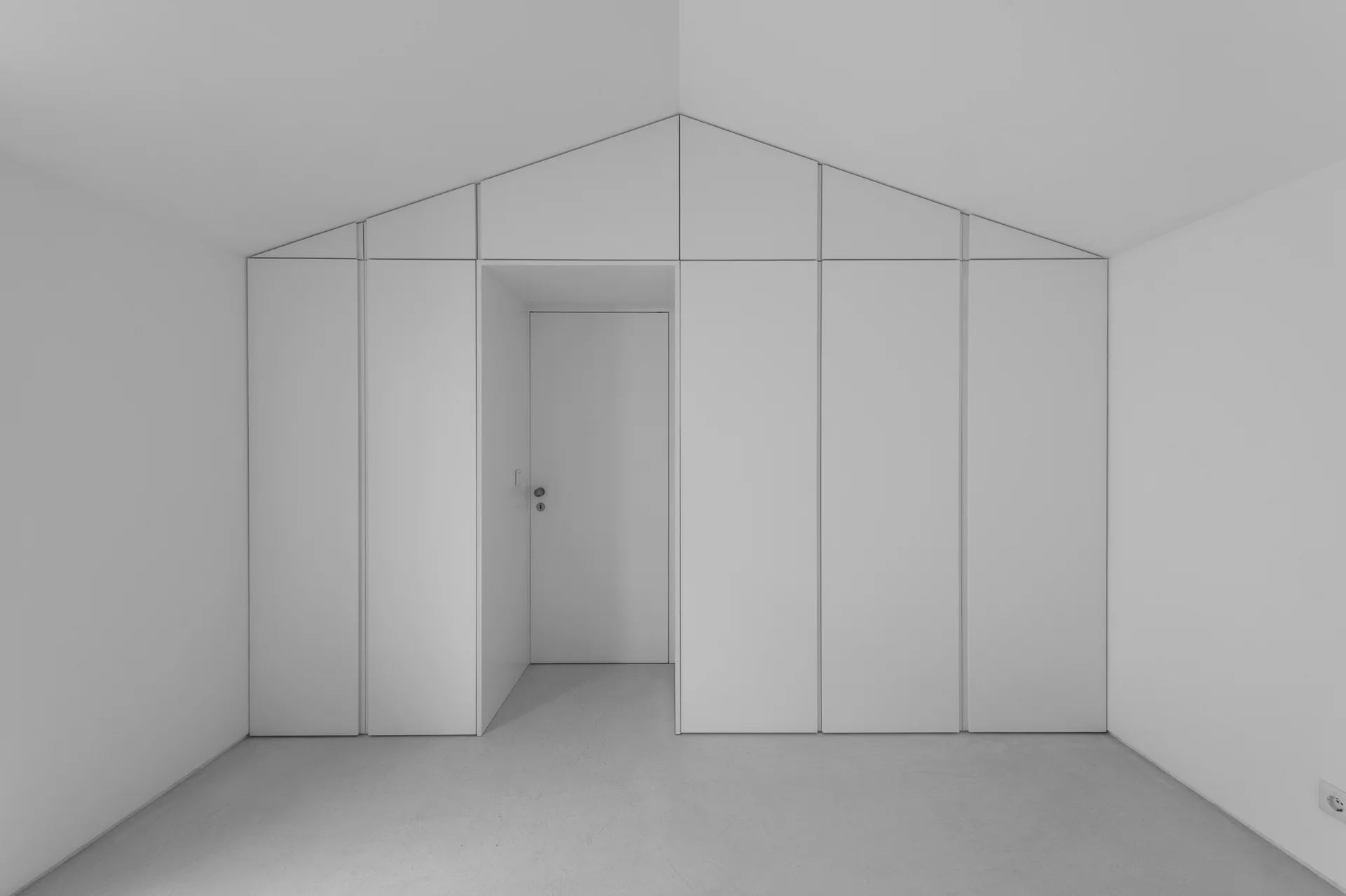 A minimalist white closet system with flat-panel, handleless doors built into a gabled wall around a central entryway.