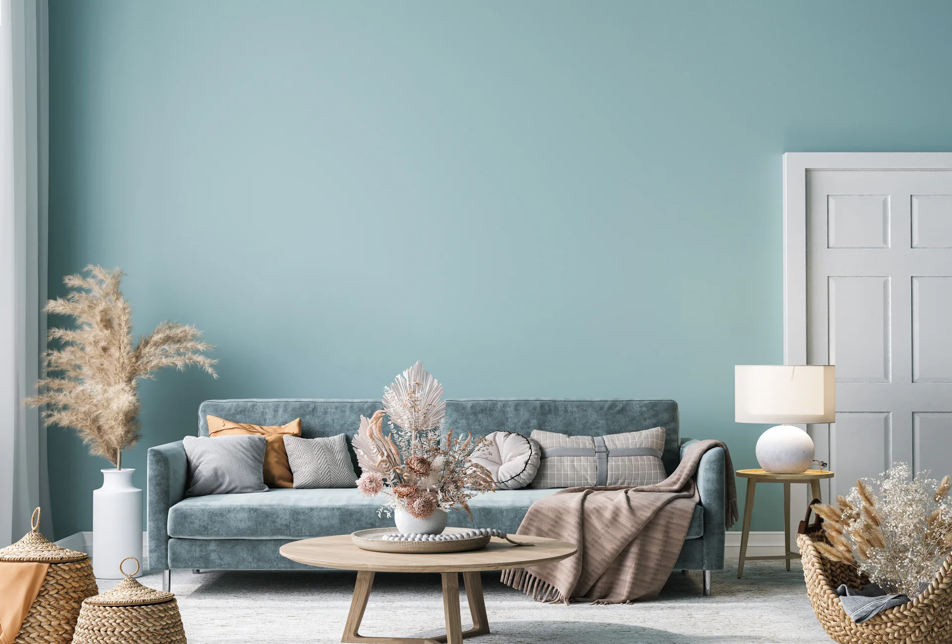 A blue velvet sofa sits against a solid teal wall next to a white door, with a round wooden coffee table and woven floor baskets.
