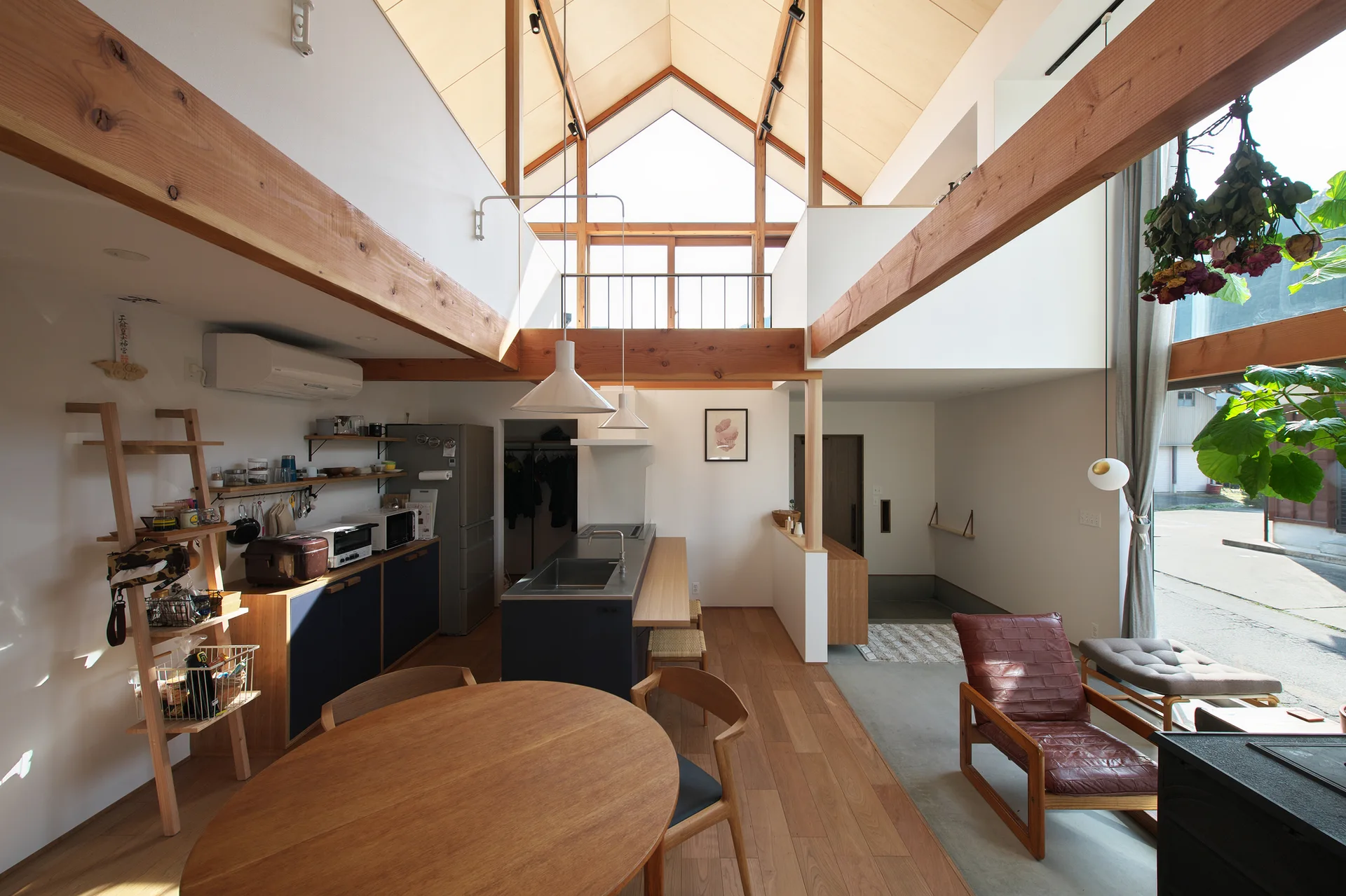 An open-concept kitchen and dining area under a double-height vaulted wood ceiling with exposed beams, a central island, and a round wooden table.