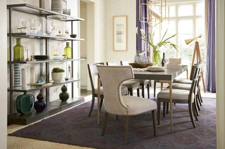 A formal dining room features a dark rectangular table, upholstered chairs, an open metal display shelf, purple curtains, and a patterned rug.