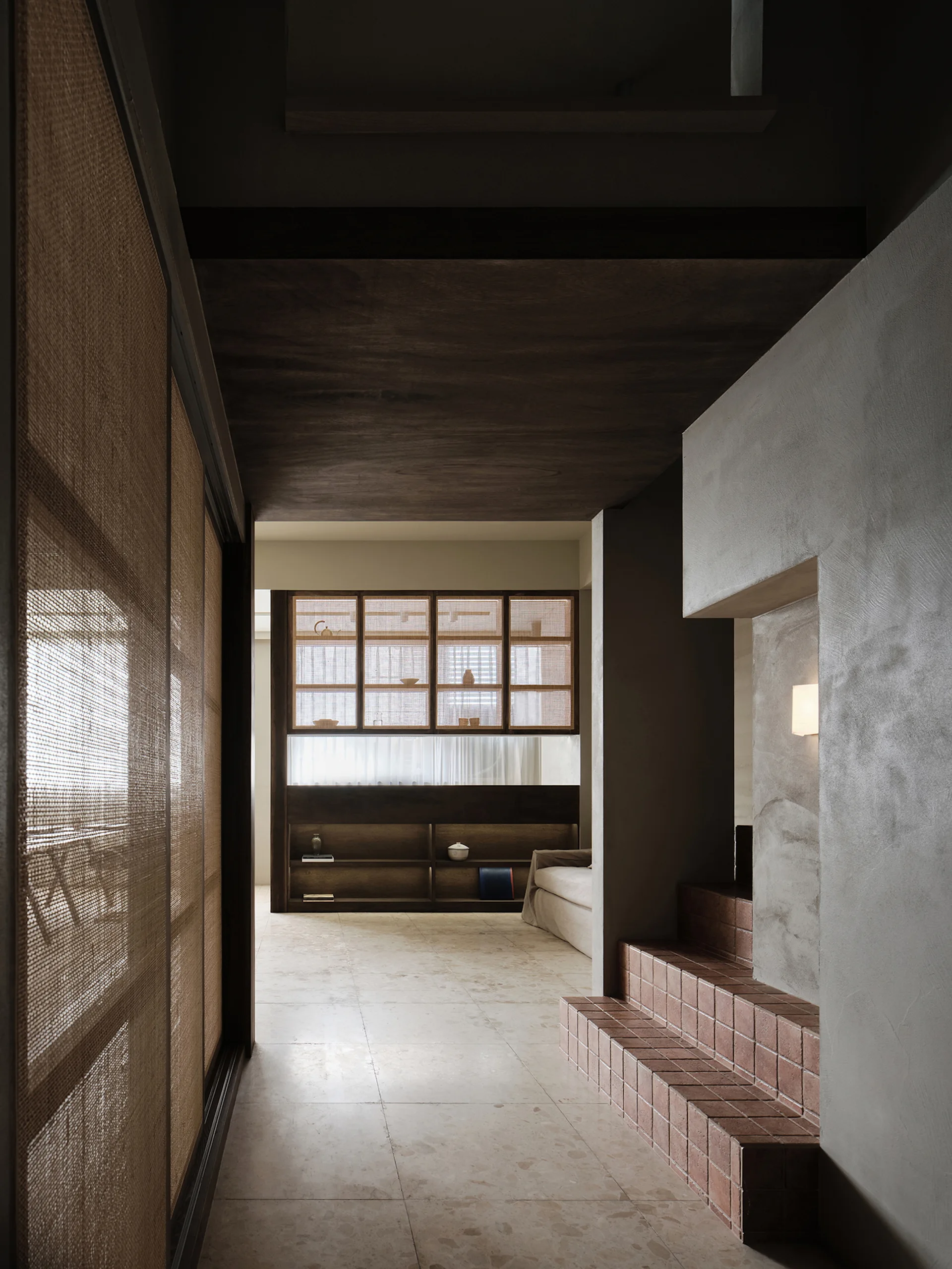 A residential hallway features textured plaster walls, terracotta-tiled steps, a dark wood ceiling, and sliding doors with woven mesh inserts.