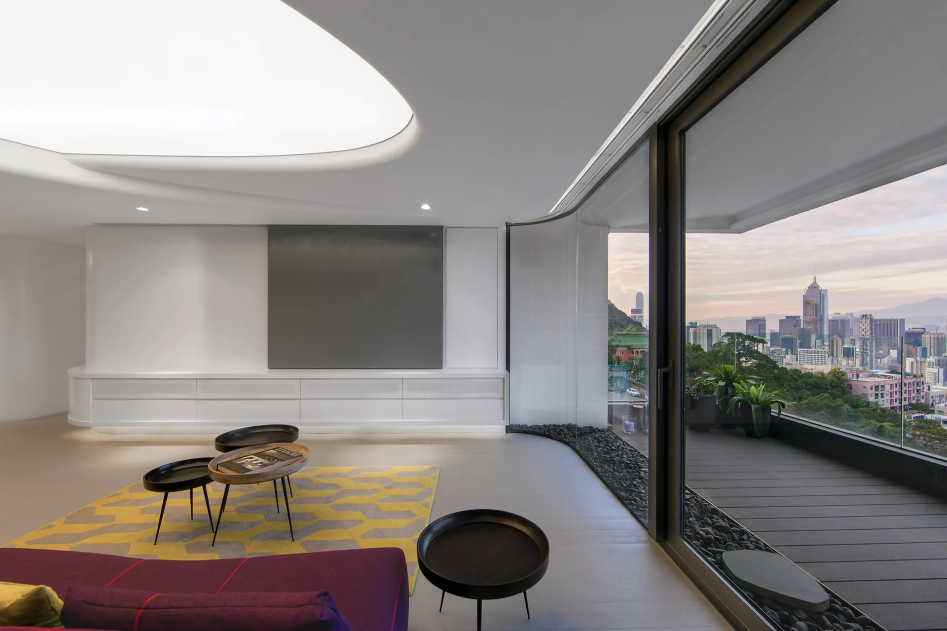A minimalist living room with a purple sofa, a yellow geometric rug, and a curved glass wall opening to a balcony with city views.