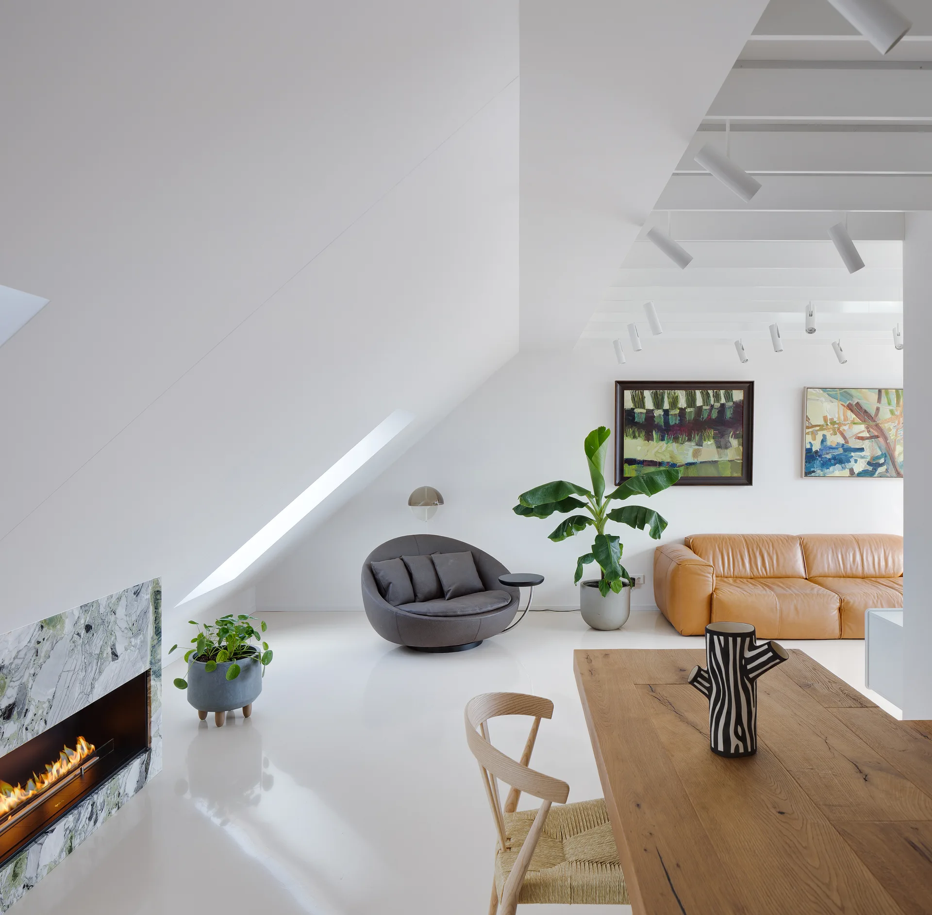 A bright attic living space features a sloped white ceiling, a green marble fireplace, a tan leather sofa, and reflective white floors.