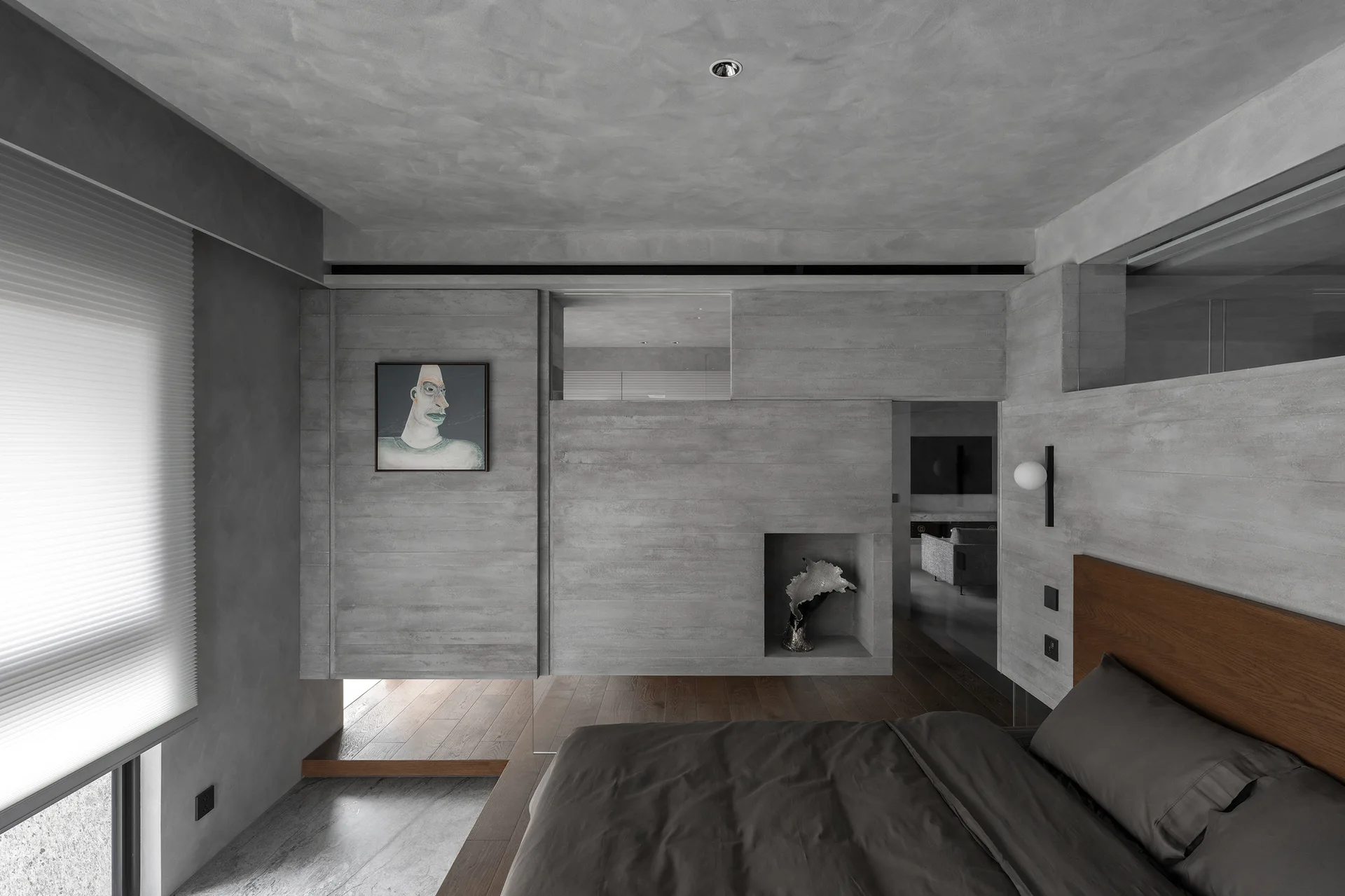 A minimalist grey concrete bedroom featuring a wooden headboard, a low bed, a wall niche, and a framed portrait painting.