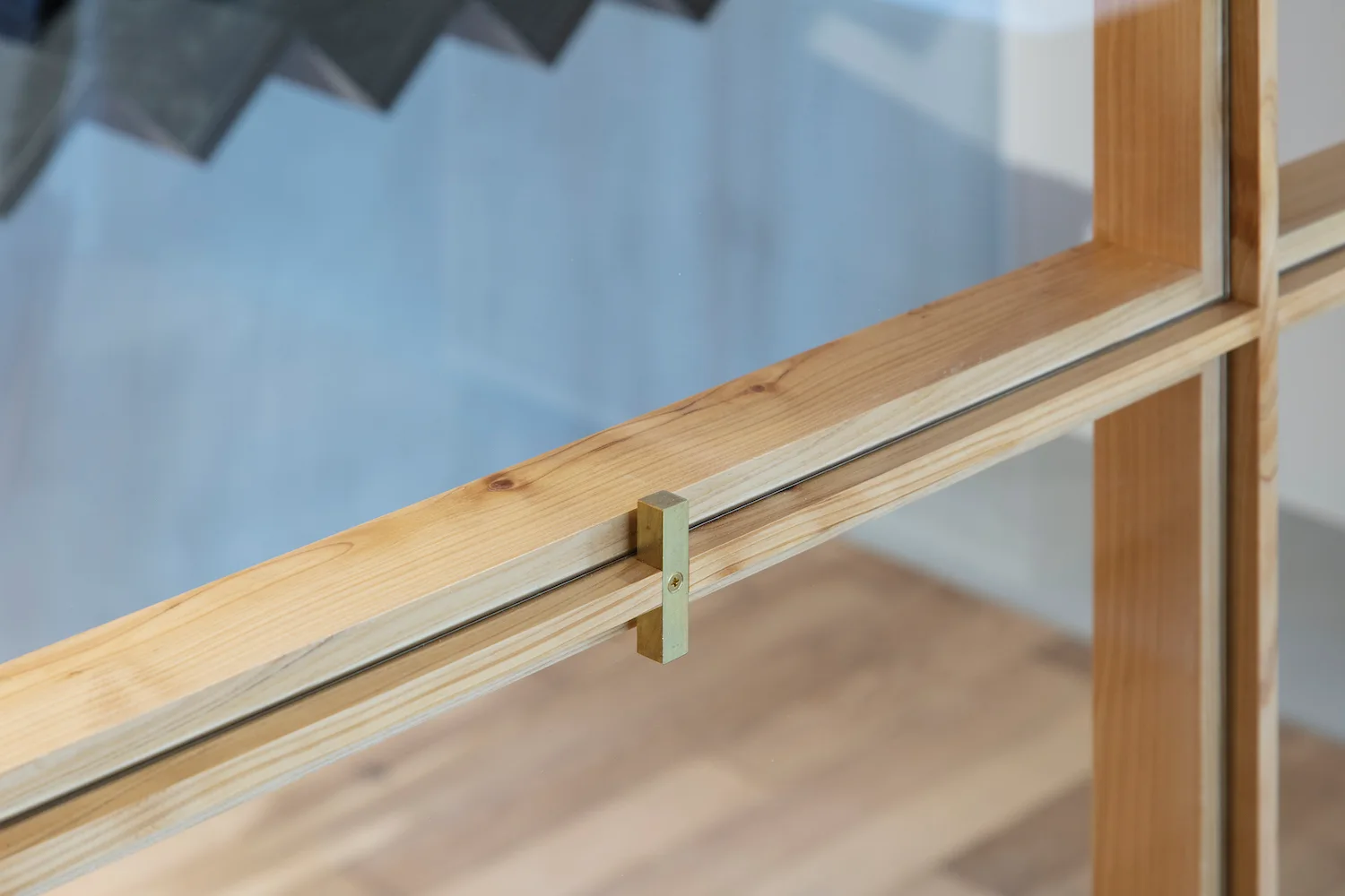 A detailed close-up of a light-toned wood window frame with glass panes and a small, rectangular brass latch.