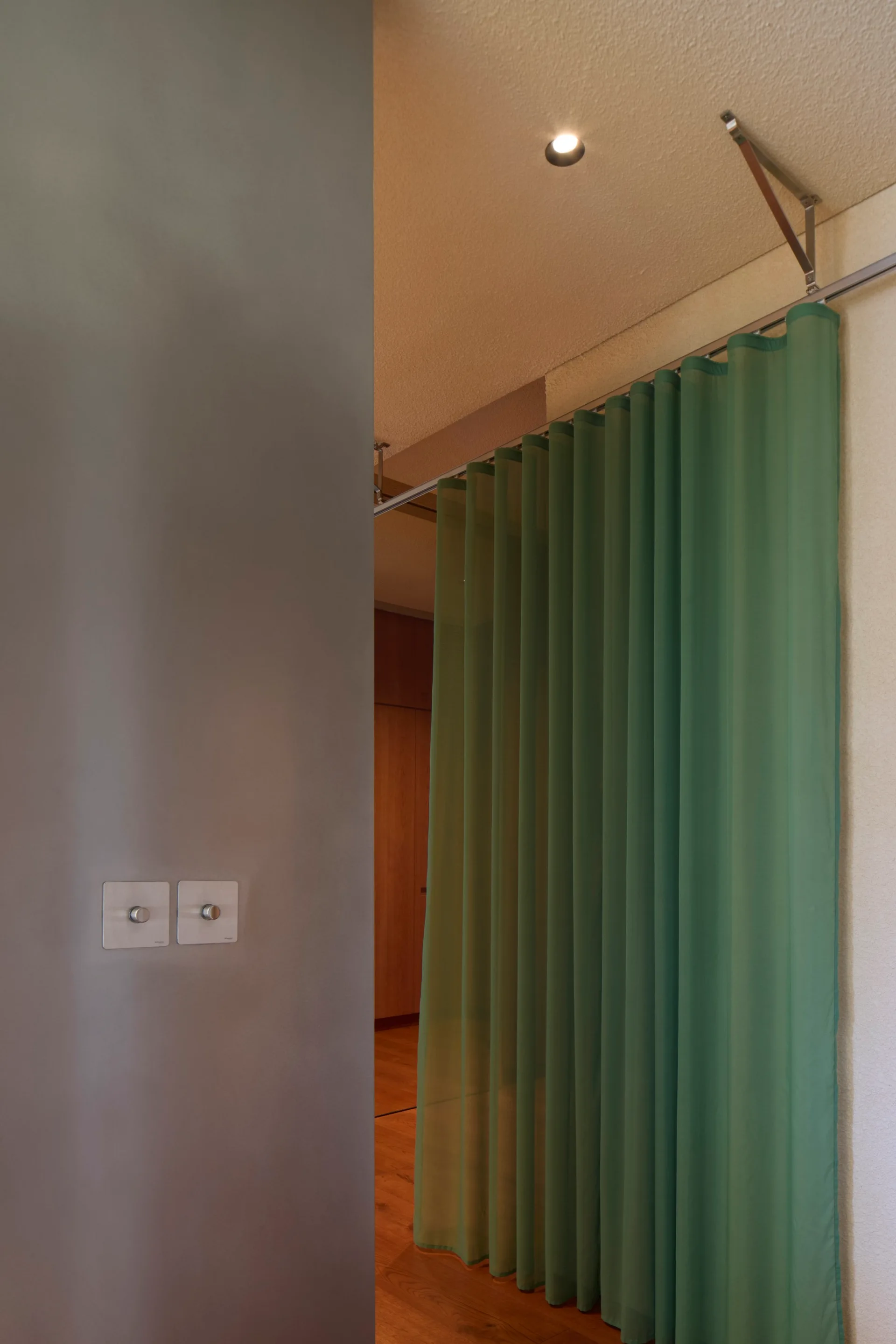 A translucent green fabric curtain hangs from a ceiling track to divide a room with smooth grey walls and wood flooring.