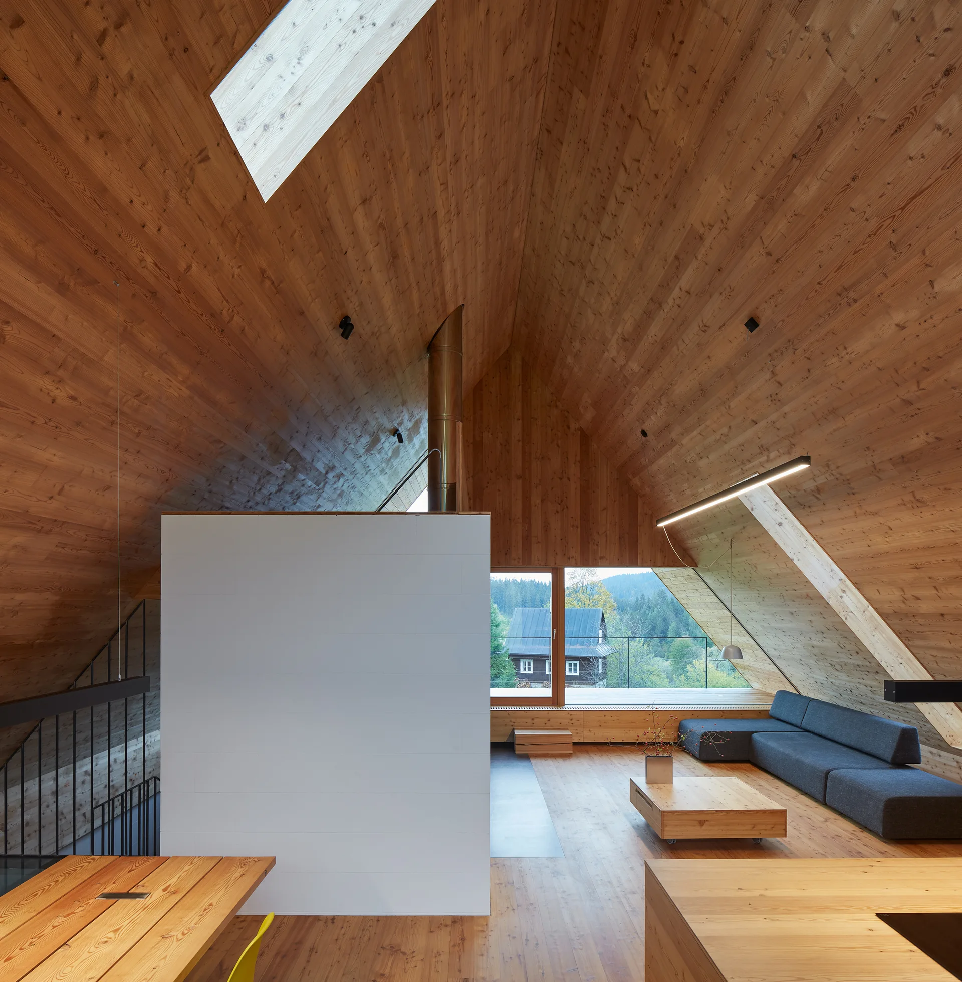 A modern attic living room features sloped wood-paneled ceilings and walls, a central white partition block, and a low-profile grey sofa.