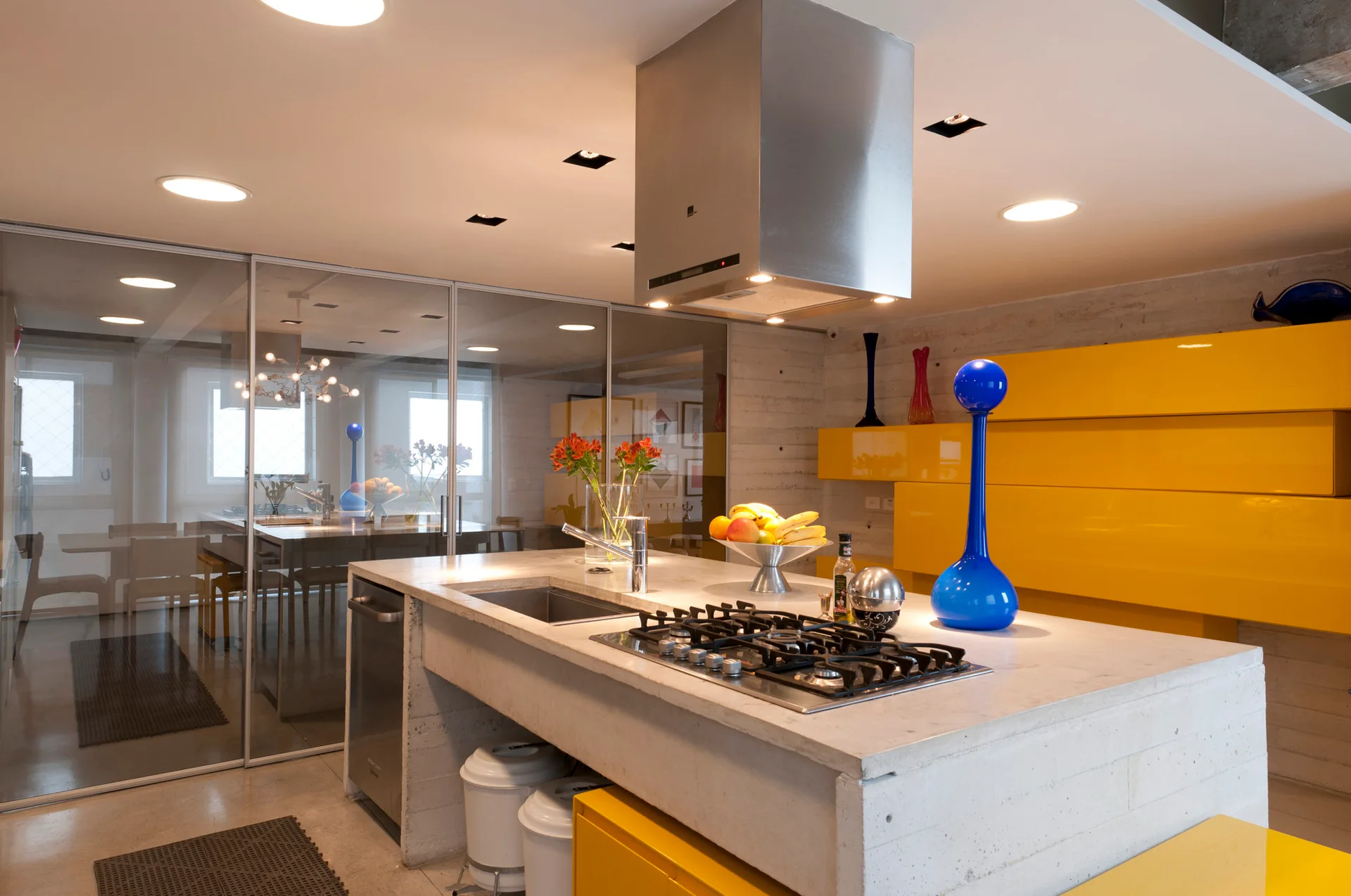 A modern kitchen featuring a textured concrete island, glossy yellow cabinetry, and a sliding glass partition wall.