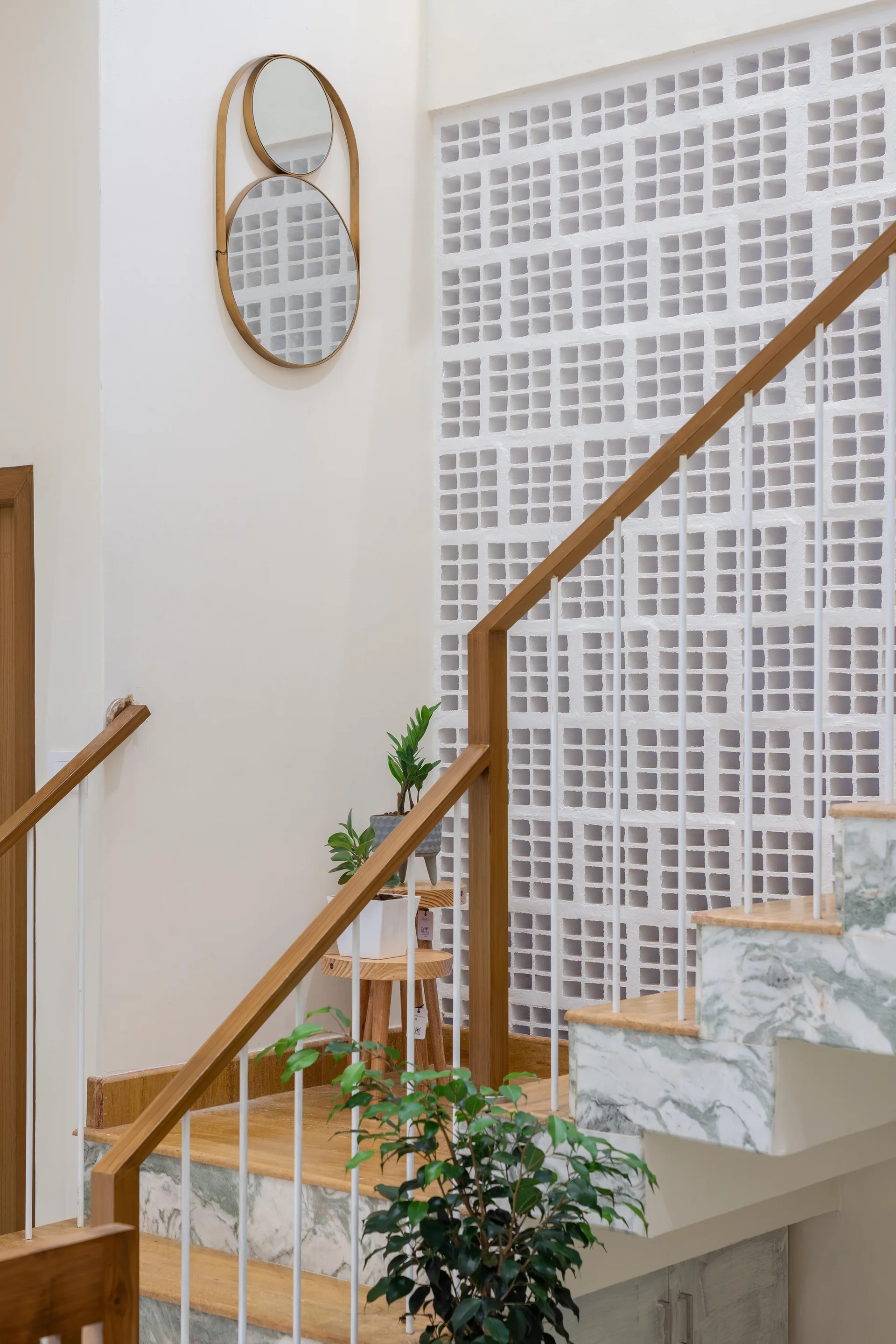 A modern staircase features green marble risers and wood treads positioned next to a geometric white breezeblock partition wall with a gold-framed mirror.