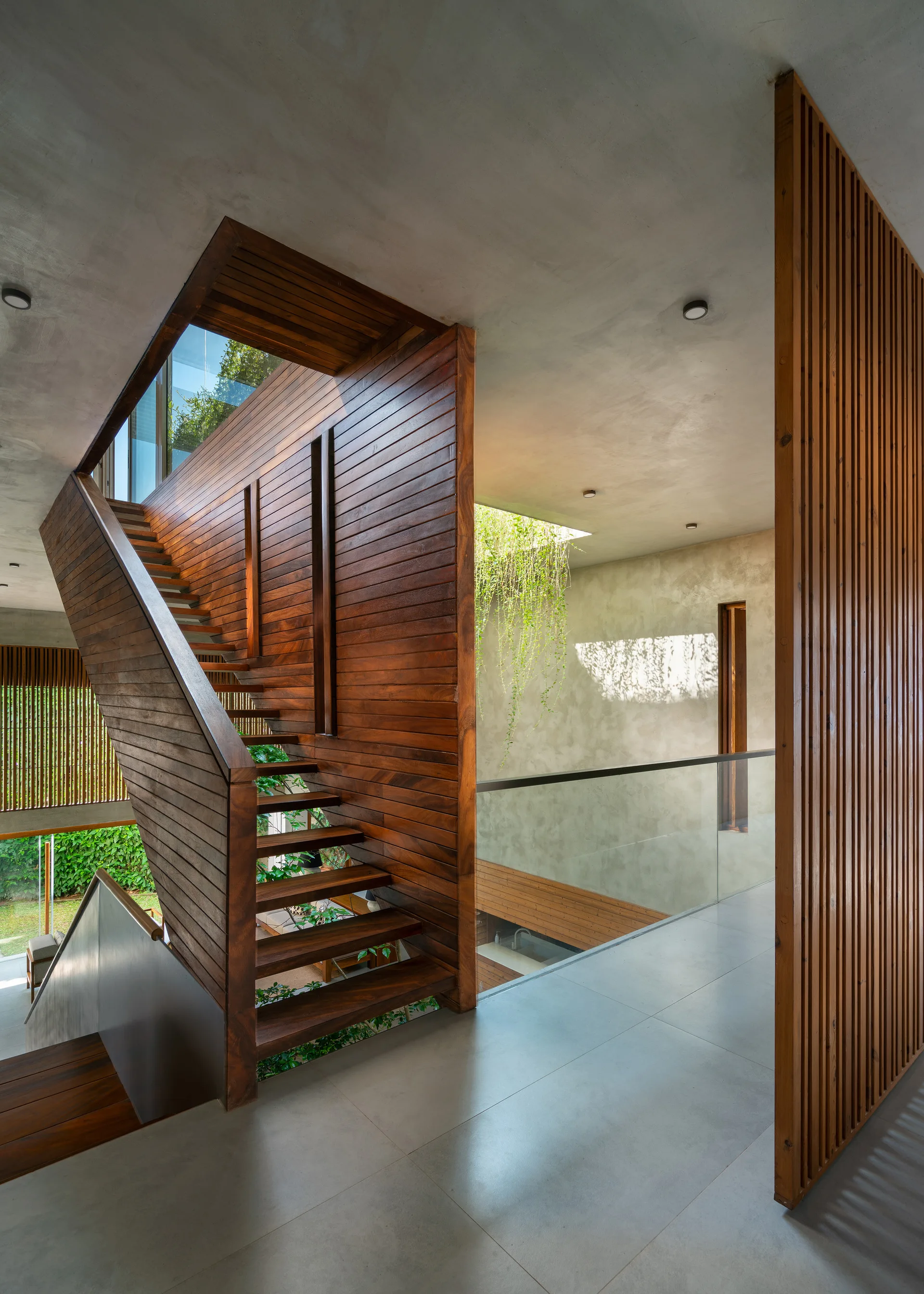 A wooden staircase with horizontal panels stands alongside a glass railing and raw concrete walls in a modern interior.