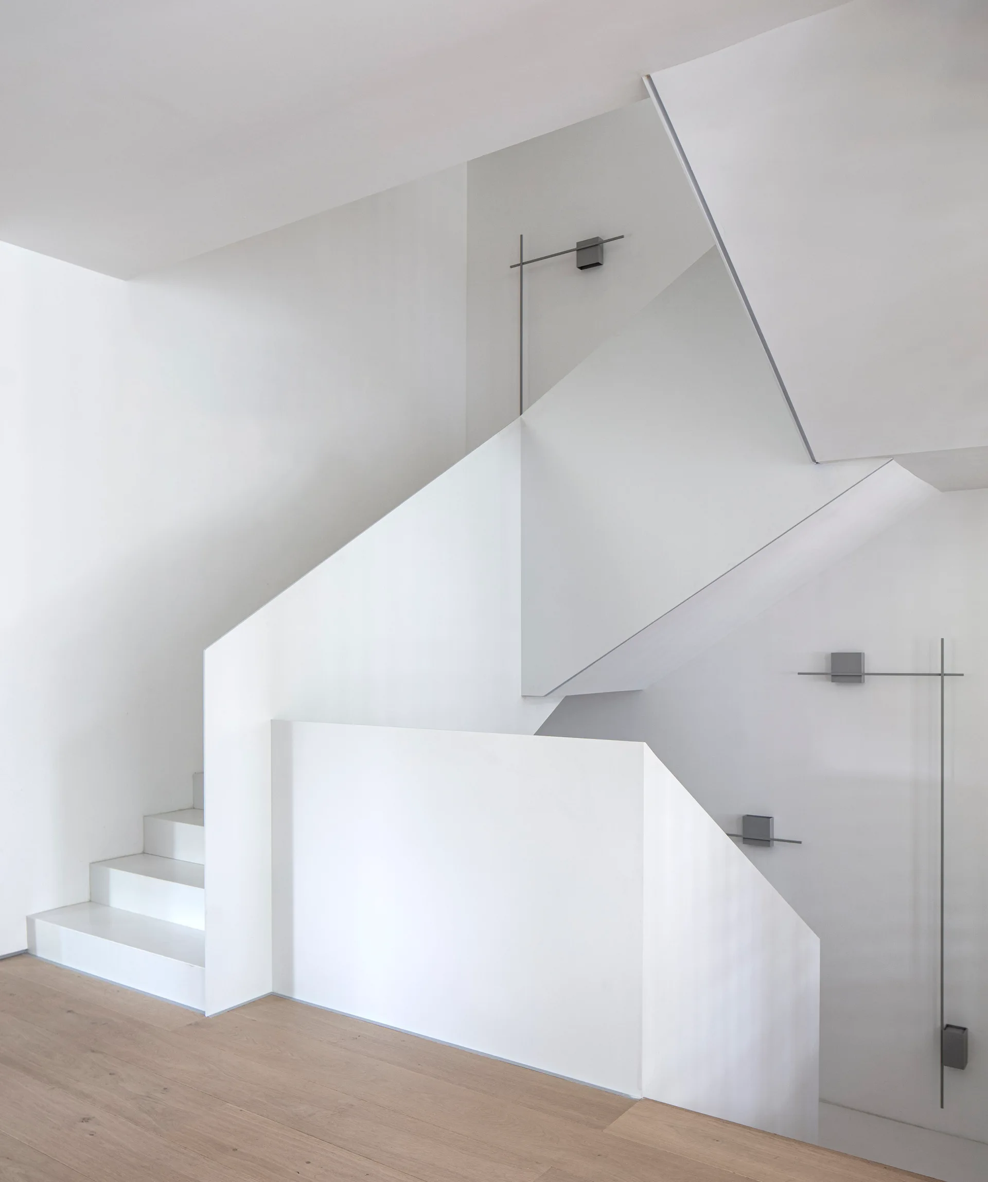 A minimalist white staircase with solid panel railings features light wood flooring and thin grey linear light fixtures on the walls.