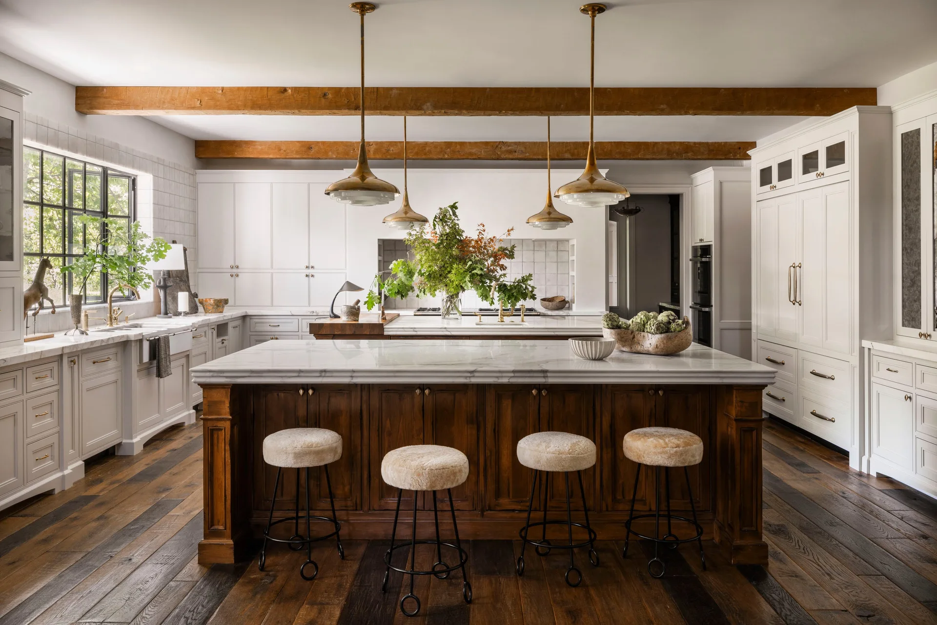 A transitional kitchen with a dark wood island, white marble countertops, white cabinets, and exposed wood ceiling beams.