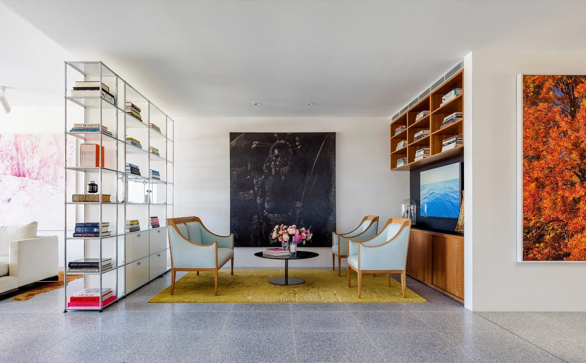Three light blue armchairs sit on a yellow rug around a black coffee table in a modern living room with modular shelving.