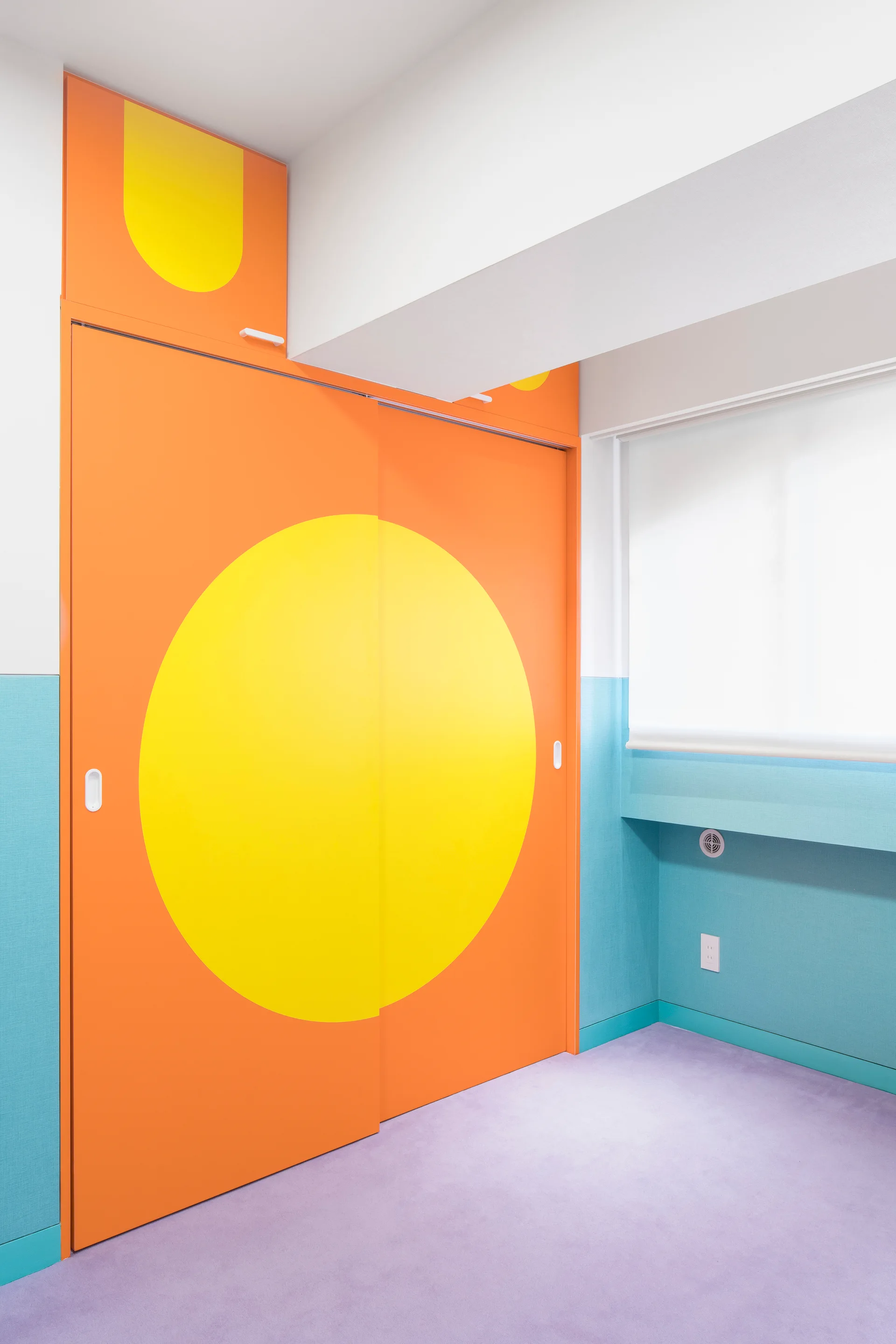 A kids bedroom featuring orange sliding closet doors decorated with a large yellow circle, blue paneled walls, and a purple carpeted floor.