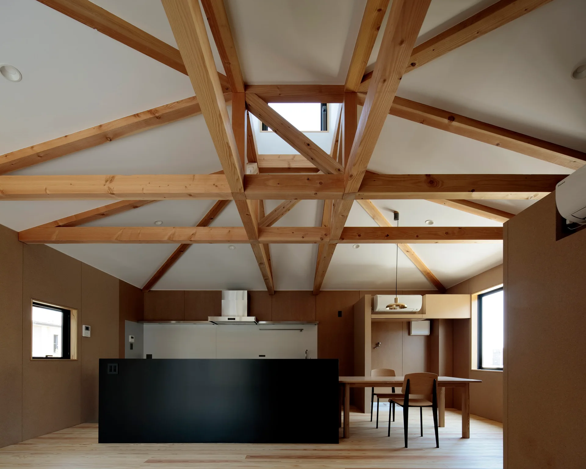 A minimalist kitchen features a large exposed wood truss ceiling with a skylight, a solid black kitchen island, and light wood floors.