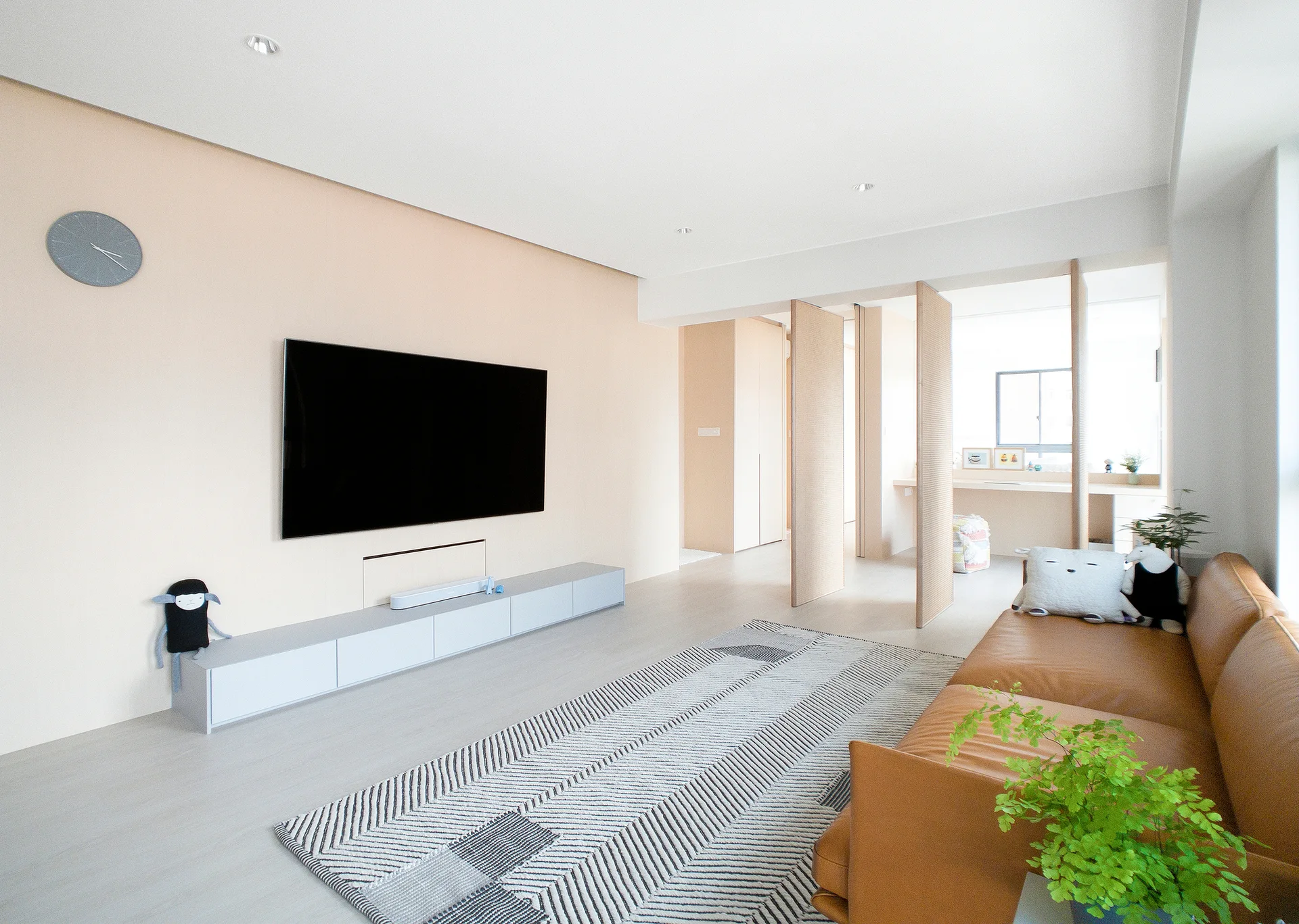 A minimalist living room features a tan leather sofa, a geometric striped rug, a wall-mounted TV, and vertical wood room divider panels.