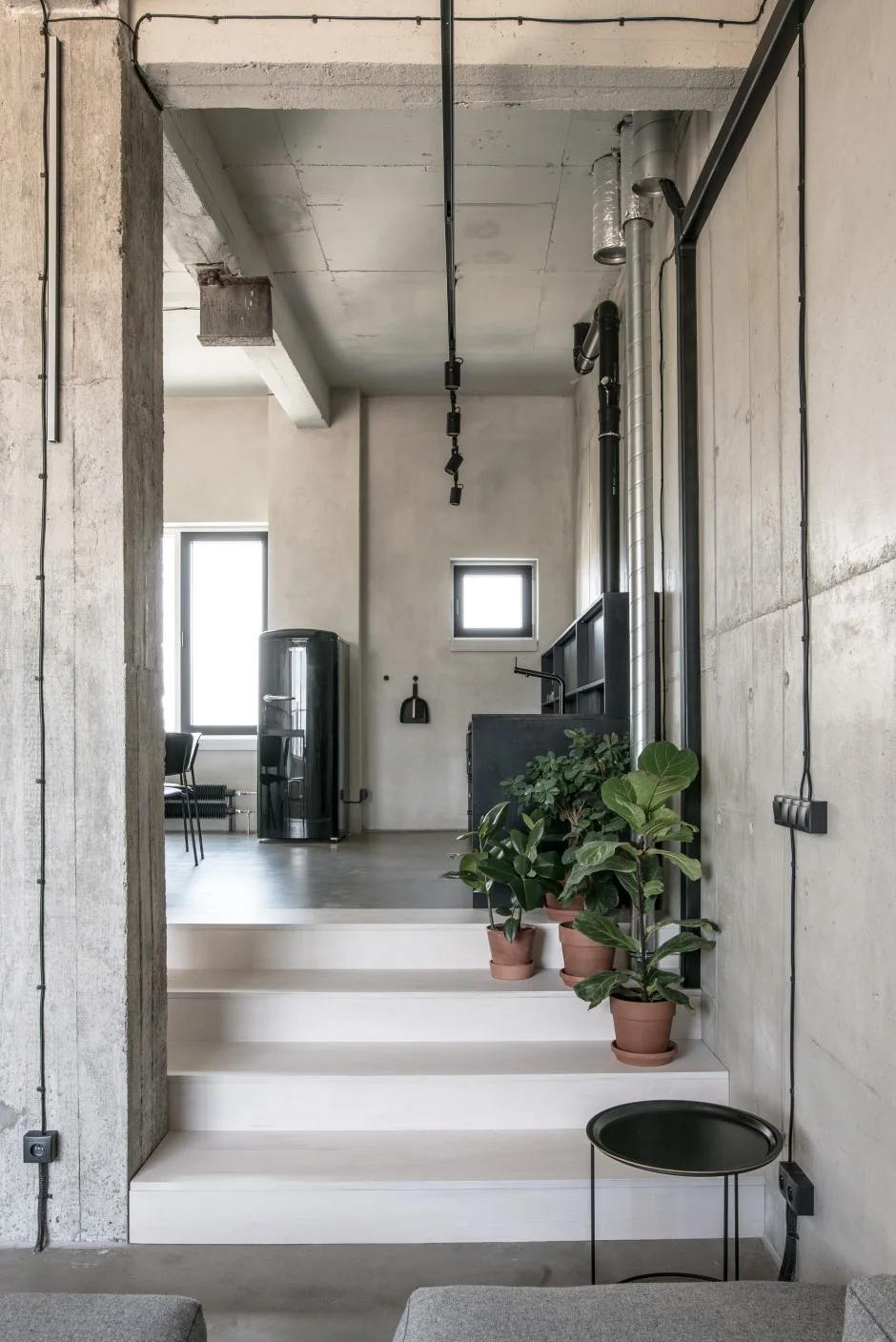White steps decorated with terracotta potted plants lead up to a raised kitchen in an industrial loft with exposed concrete walls.