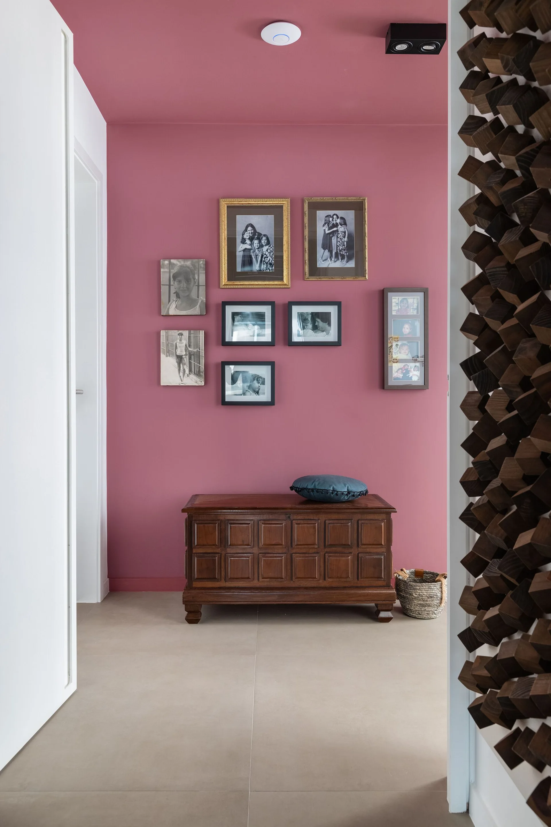 A hallway with a pink accent wall and matching ceiling features a gallery of framed photos above a vintage wooden trunk.