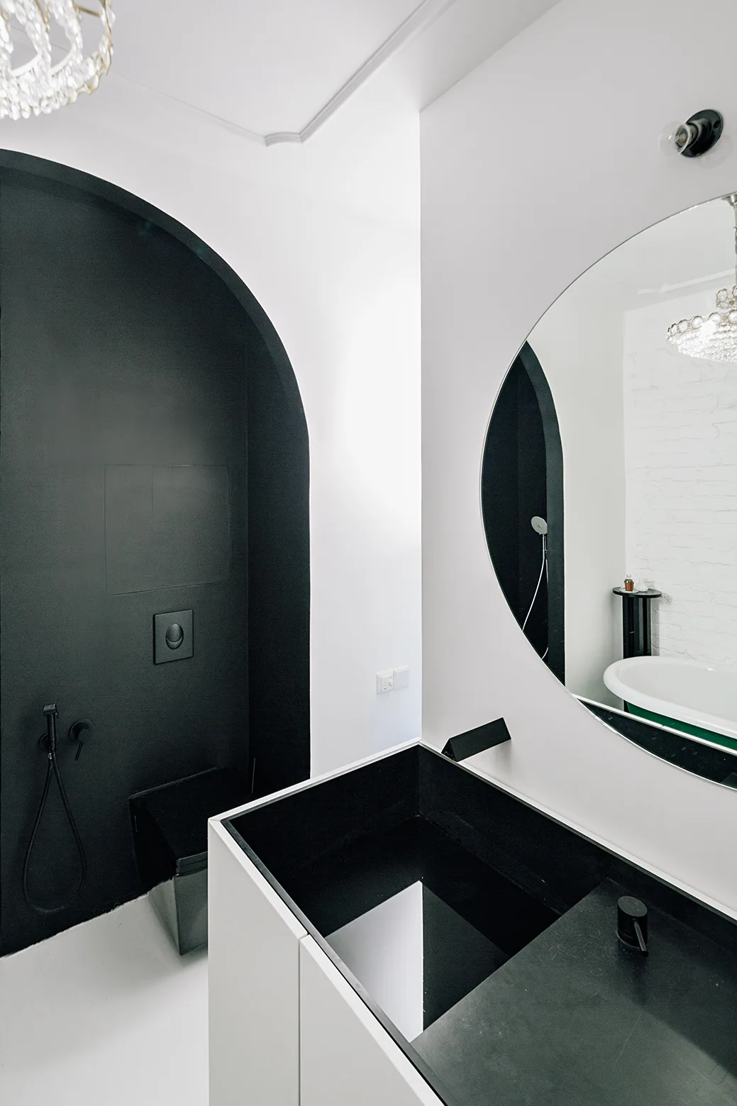 A minimalist bathroom features a black-painted arched alcove, a white vanity with an integrated black basin, and a large round wall mirror.