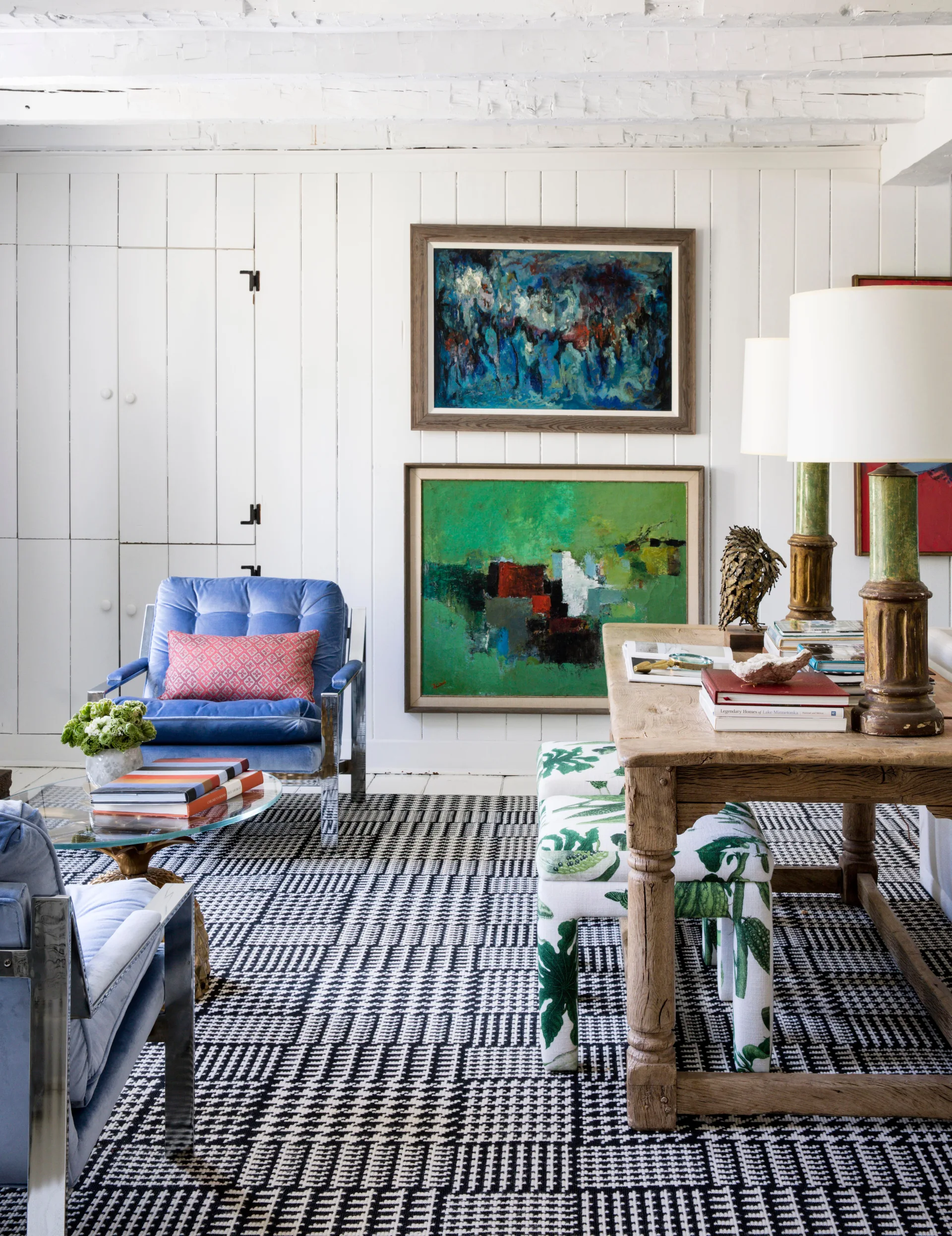 An eclectic living room featuring blue velvet armchairs, a rustic wooden table with lamps, and a bold black and white houndstooth patterned rug.