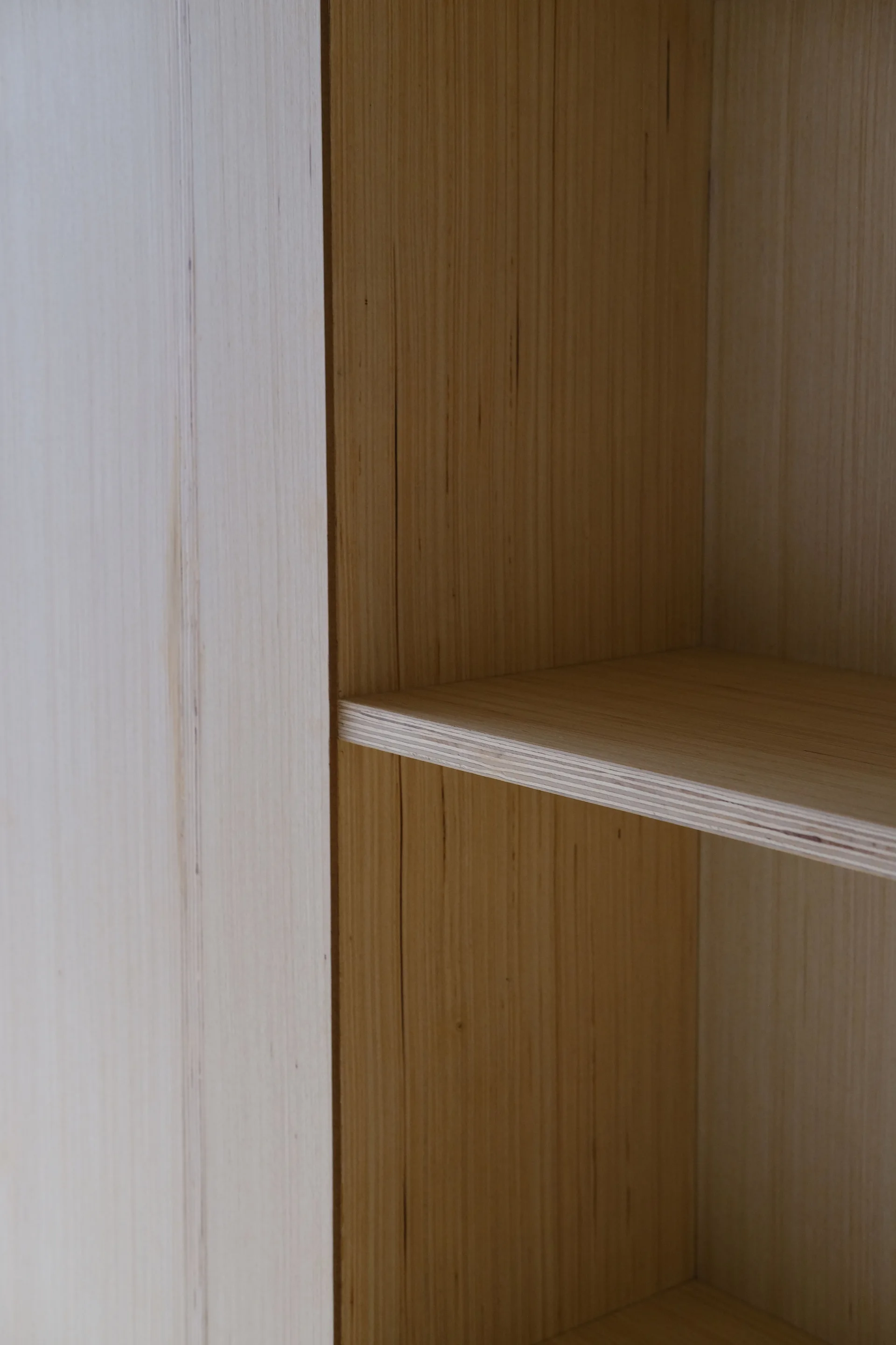 A close-up of a light wood plywood shelving unit showing the vertical grain and the horizontal shelf with an exposed layered edge.