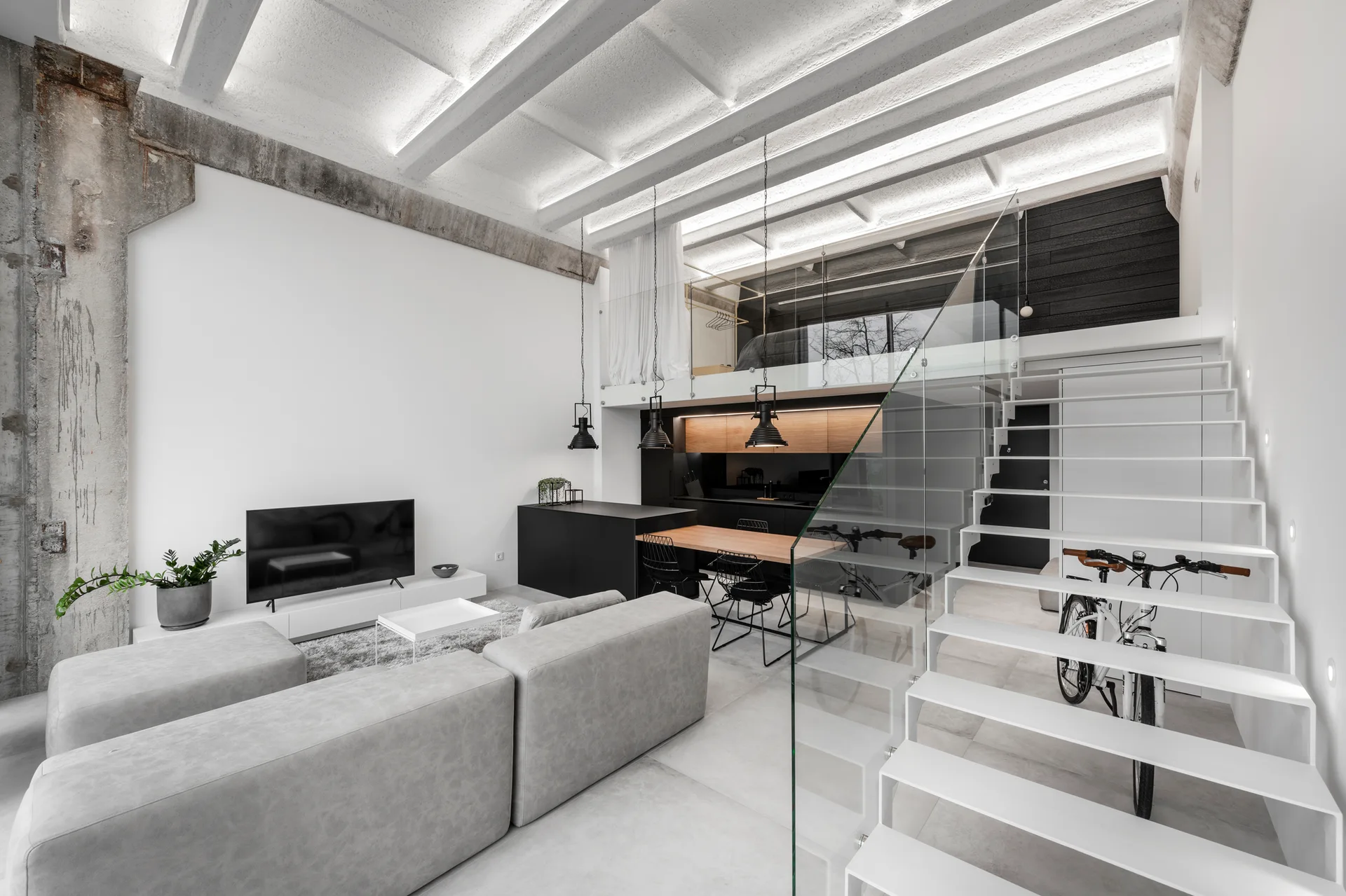 A minimalist open-plan loft featuring a modular grey sofa, a sleek white floating staircase with a glass railing, and an exposed concrete ceiling.