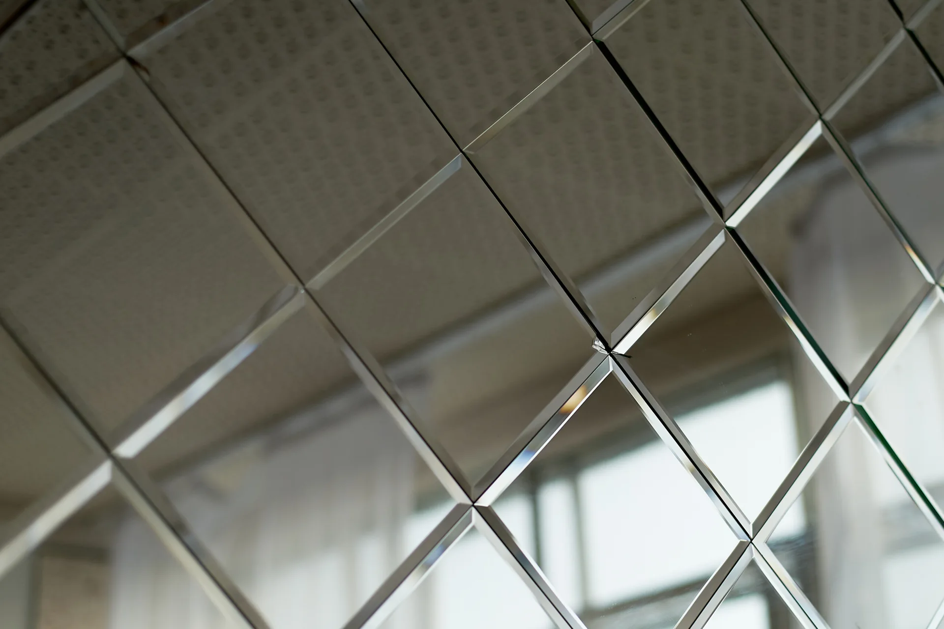 A close-up of a mirrored wall made of diamond-shaped tiles with beveled edges that catch the light.