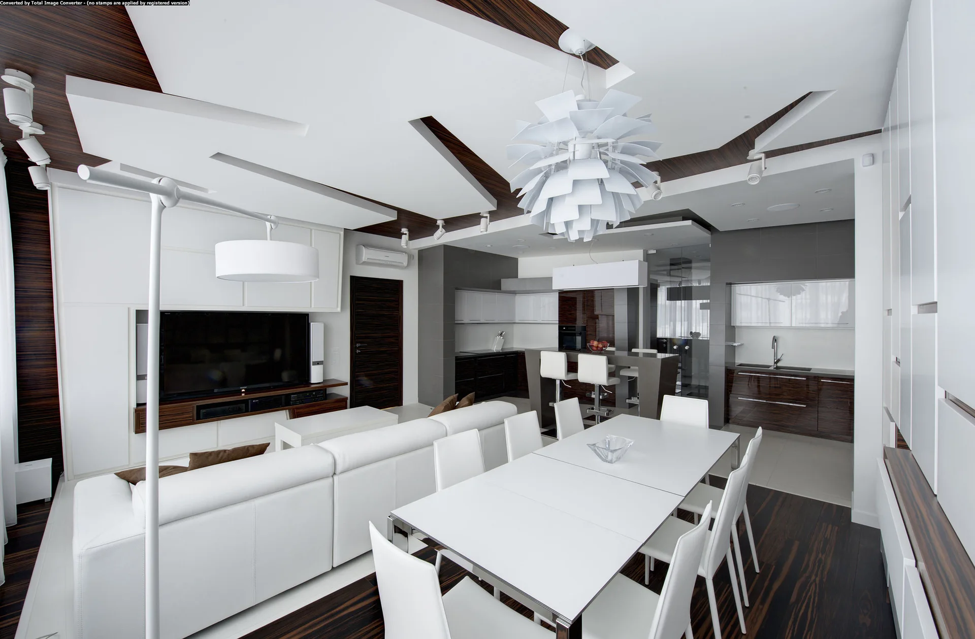 A modern open-concept living and dining area with a white sectional sofa, dining table, dark wood floors, and geometric wood ceiling panels.