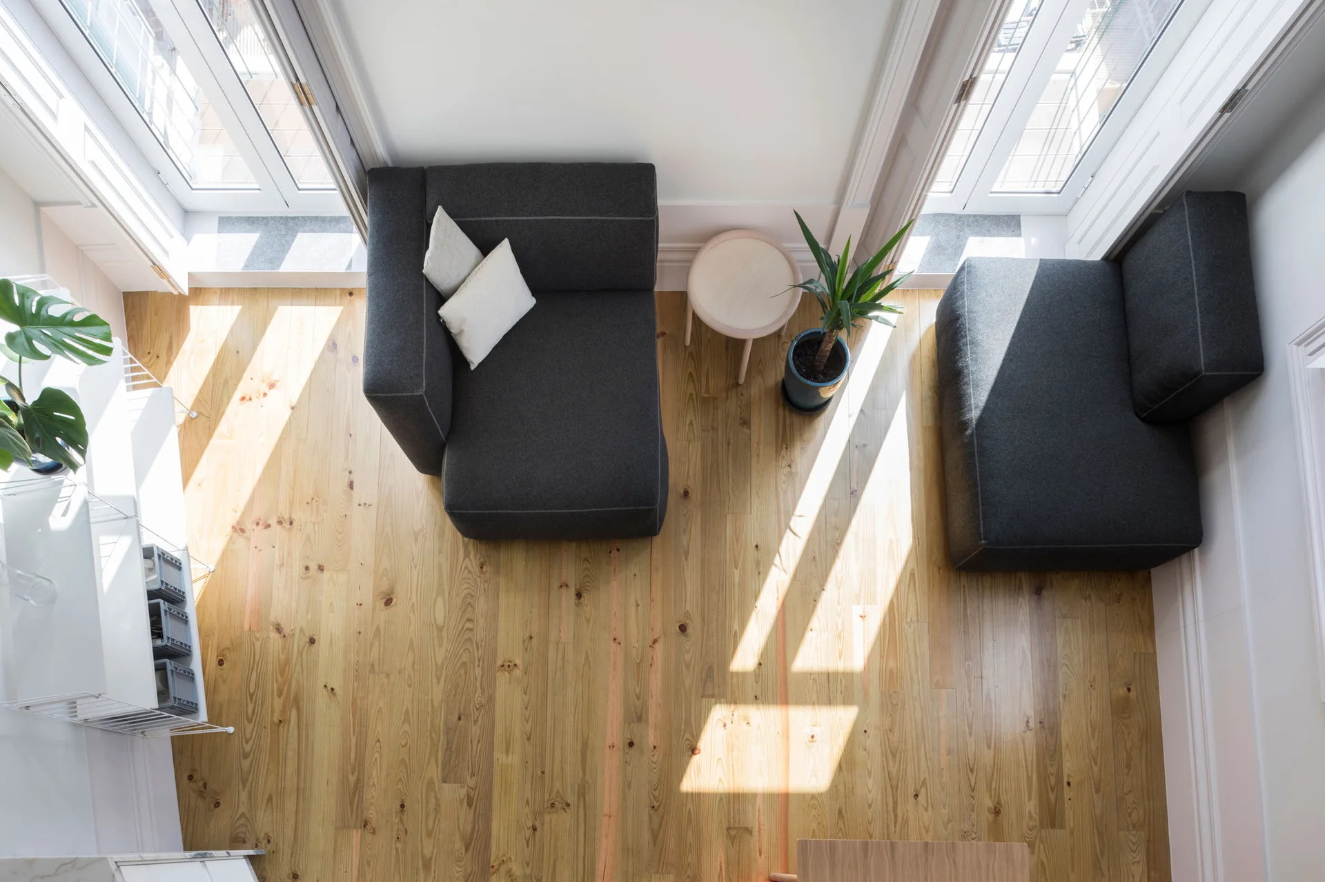 An overhead view of a bright living room featuring two dark grey armchairs, a small round wooden table, and natural wood plank flooring.
