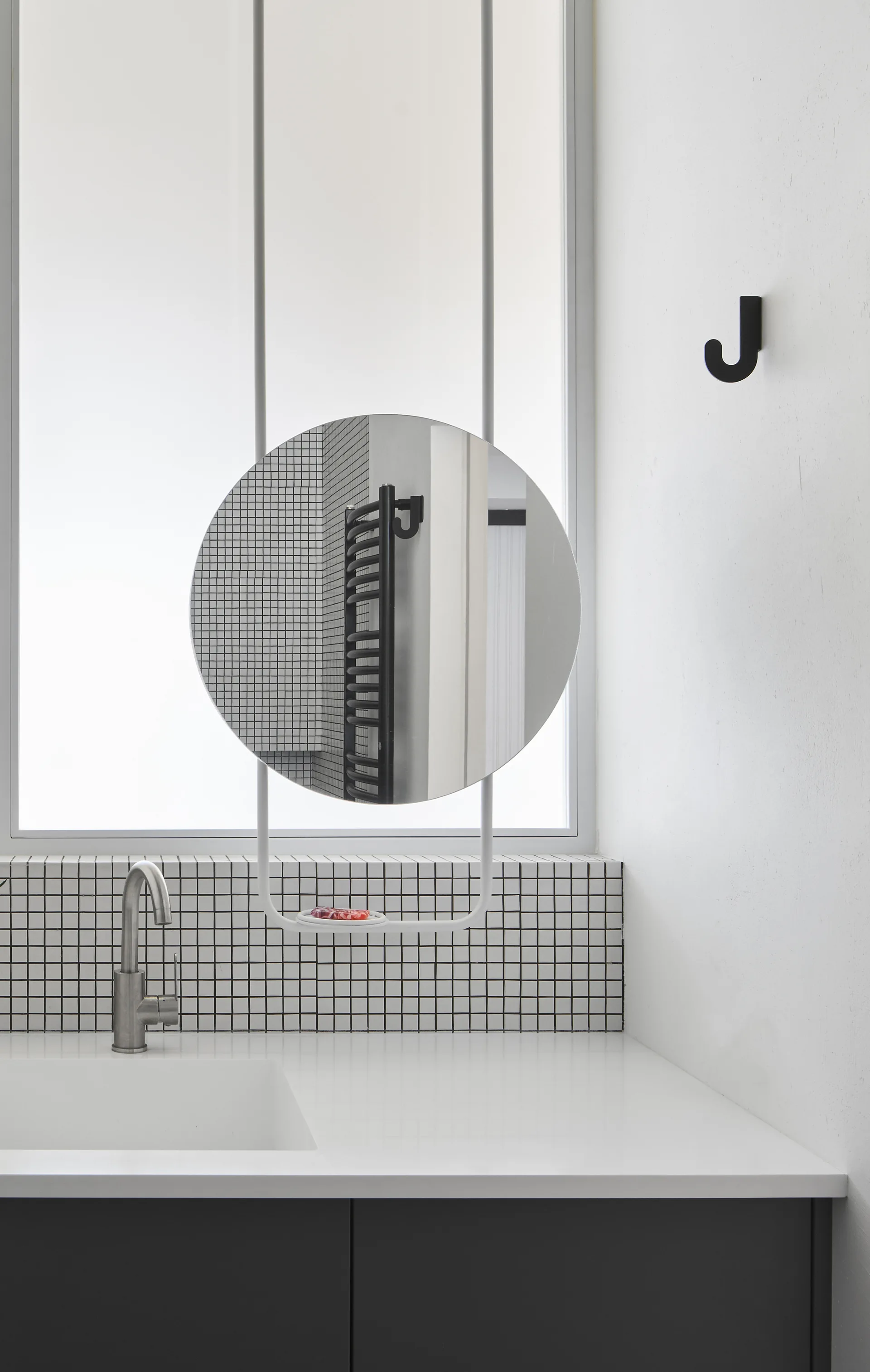 A minimalist bathroom vanity features a round mirror suspended over an integrated sink with a black-and-white grid tile backsplash.
