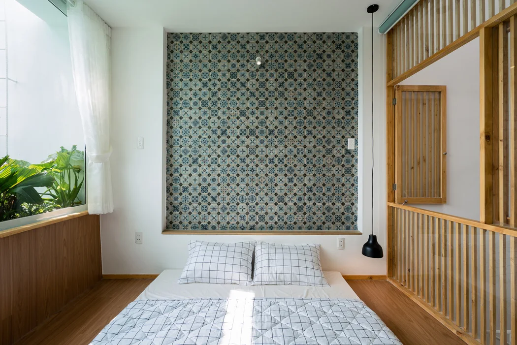 A minimalist bedroom features a low bed on wood floors, a blue tiled feature wall, and a wooden slat room divider.
