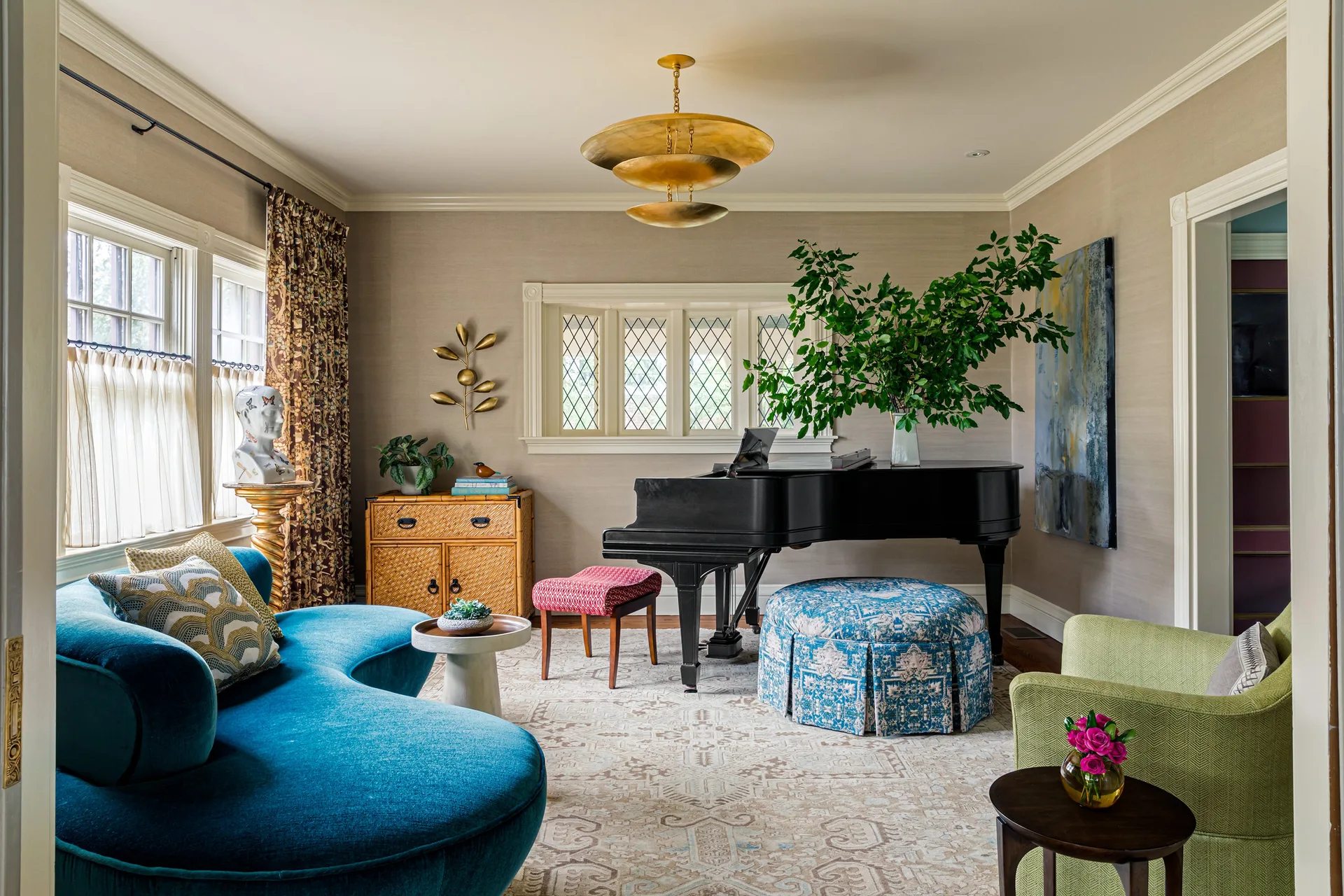 An eclectic living room features a black grand piano, a curved blue velvet sofa, and textured grasscloth wallpaper walls.