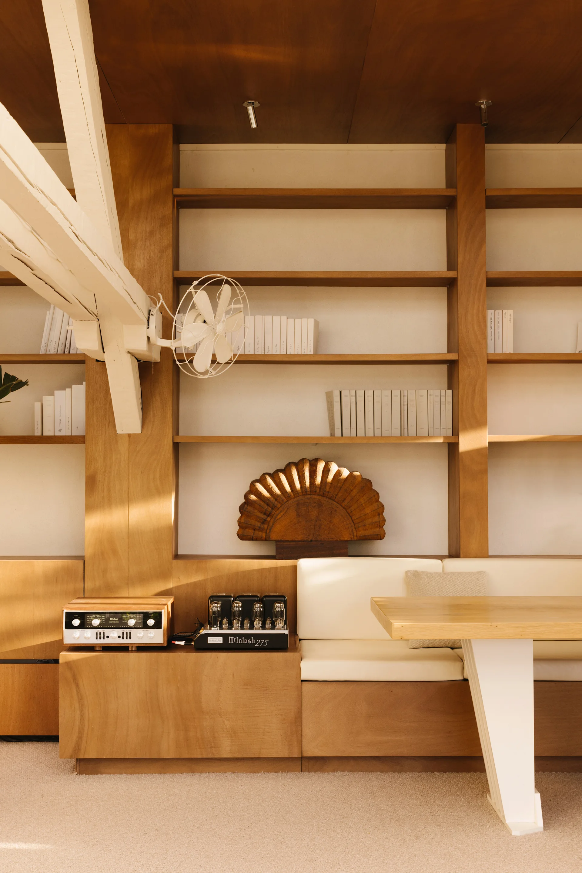A living area features warm wooden built-in shelving with integrated off-white bench seating, a wood table, and vintage-style audio equipment.