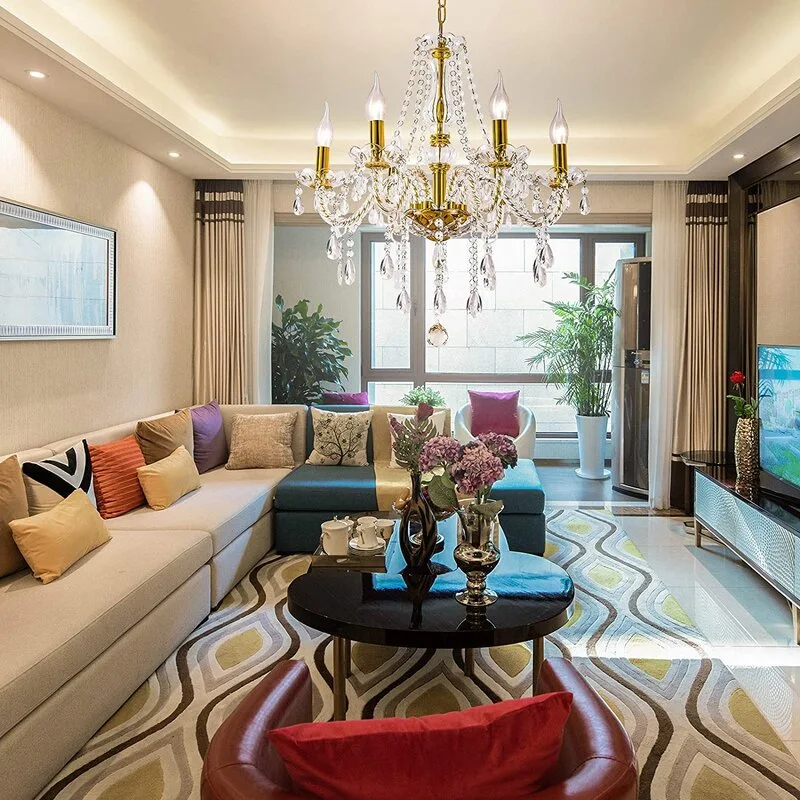 A contemporary living room features a brass crystal chandelier, a blue and cream sectional sofa, a black coffee table, and a wavy geometric area rug.