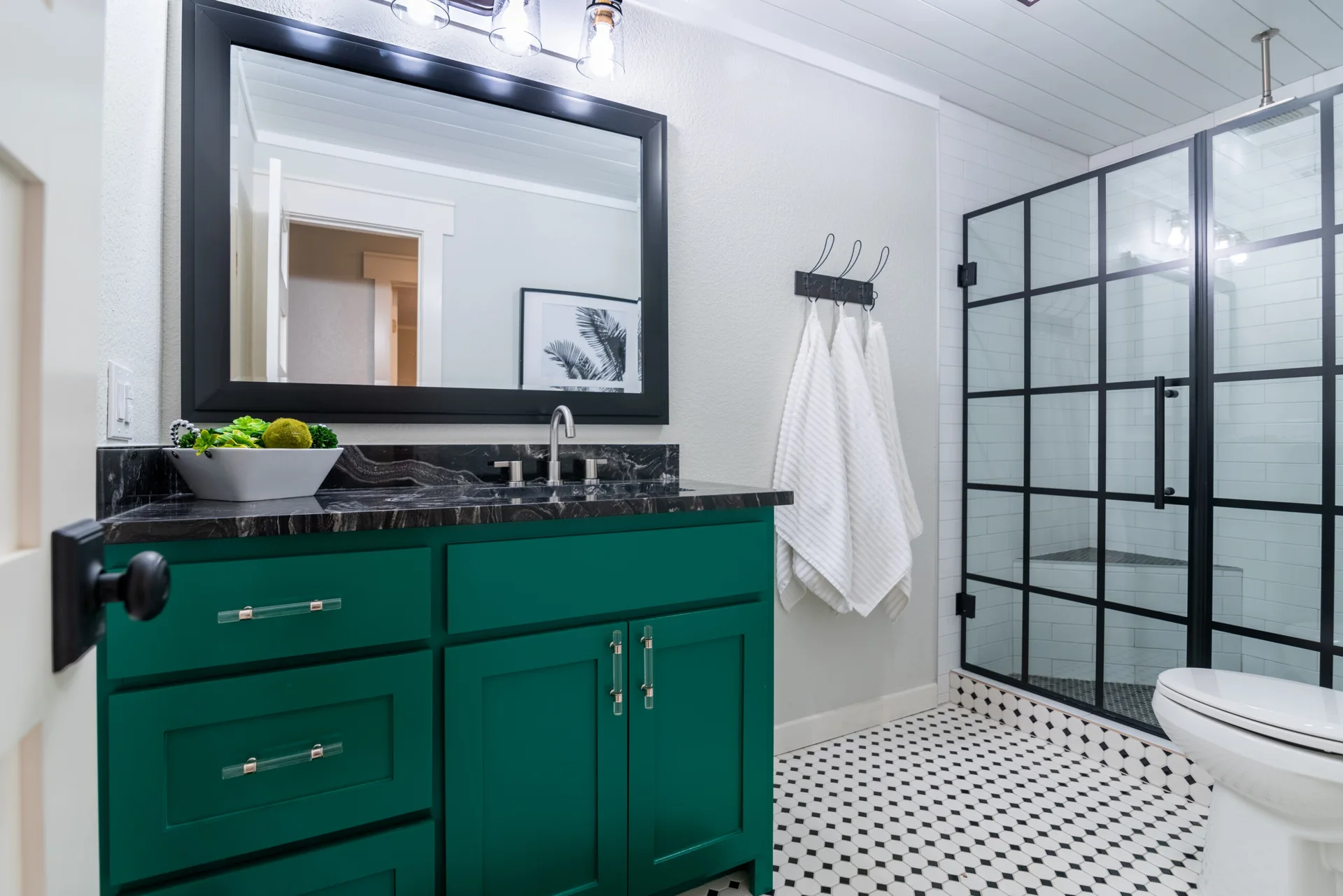 A modern bathroom showcases a bold green vanity with a dark countertop alongside a black-framed grid shower door and hexagonal floor tiles.