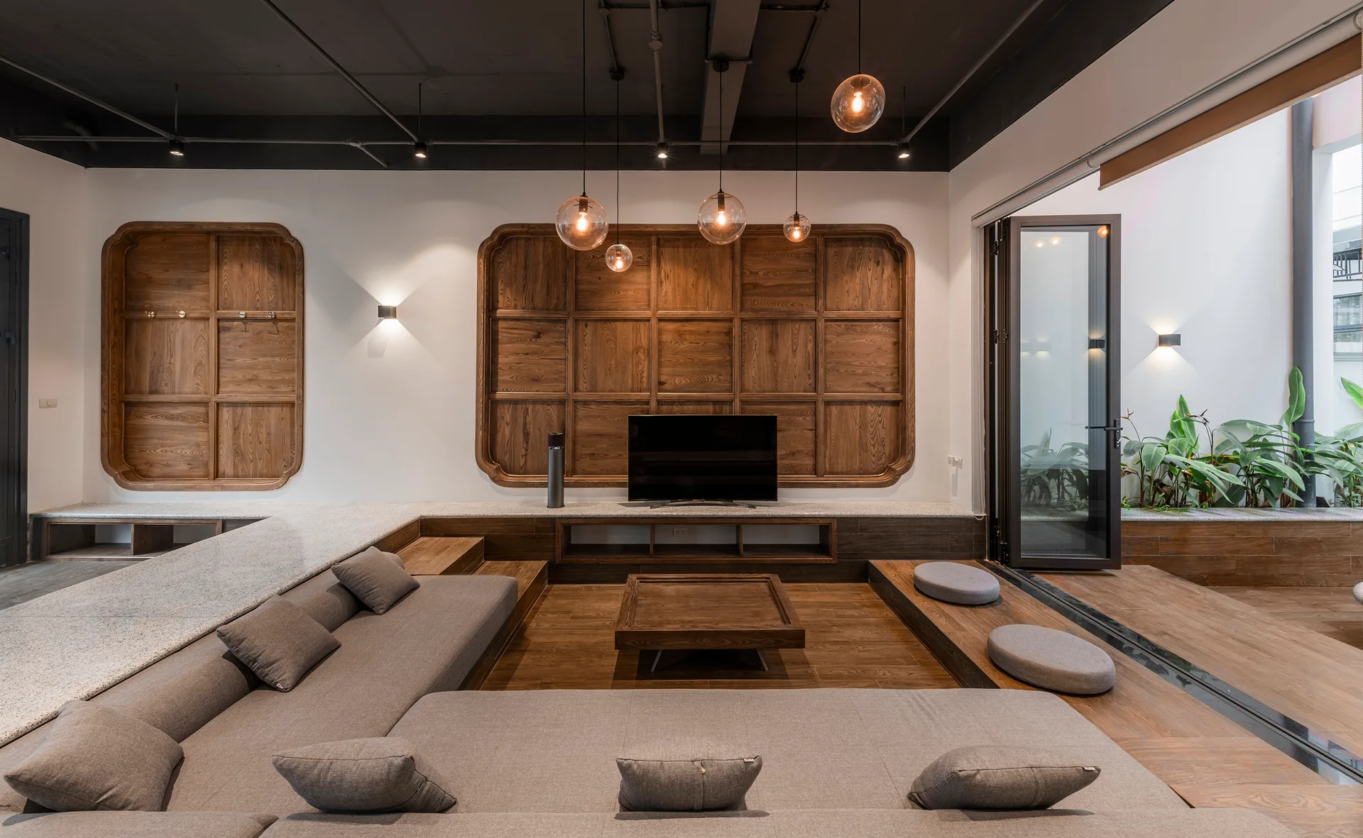 A modern sunken living room features a large grey sectional sofa, a square wood coffee table, and a grid-patterned wood panel on the wall.