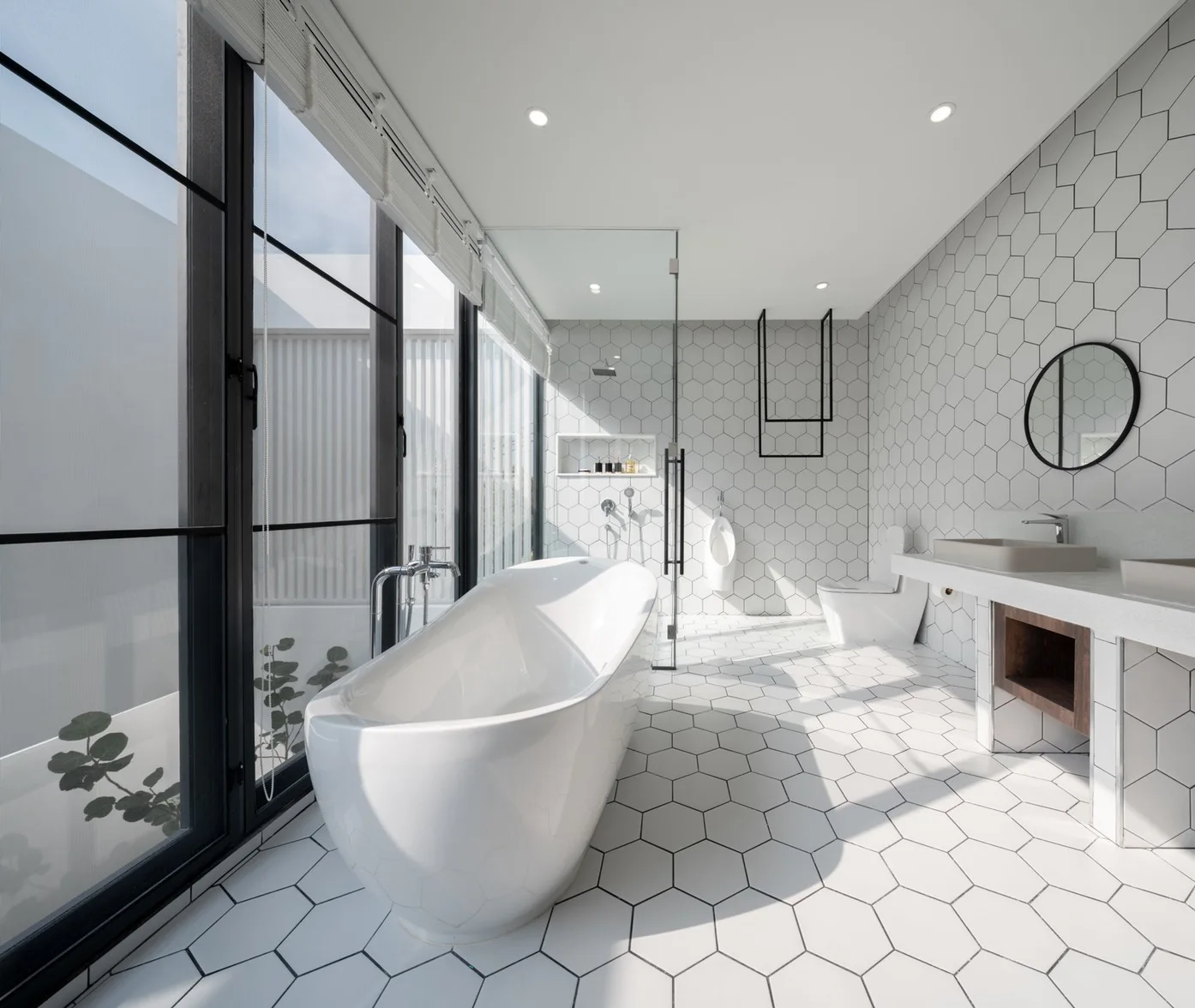 A modern white bathroom with hexagonal wall and floor tiles, a freestanding oval tub beside a large window, and a floating vanity.