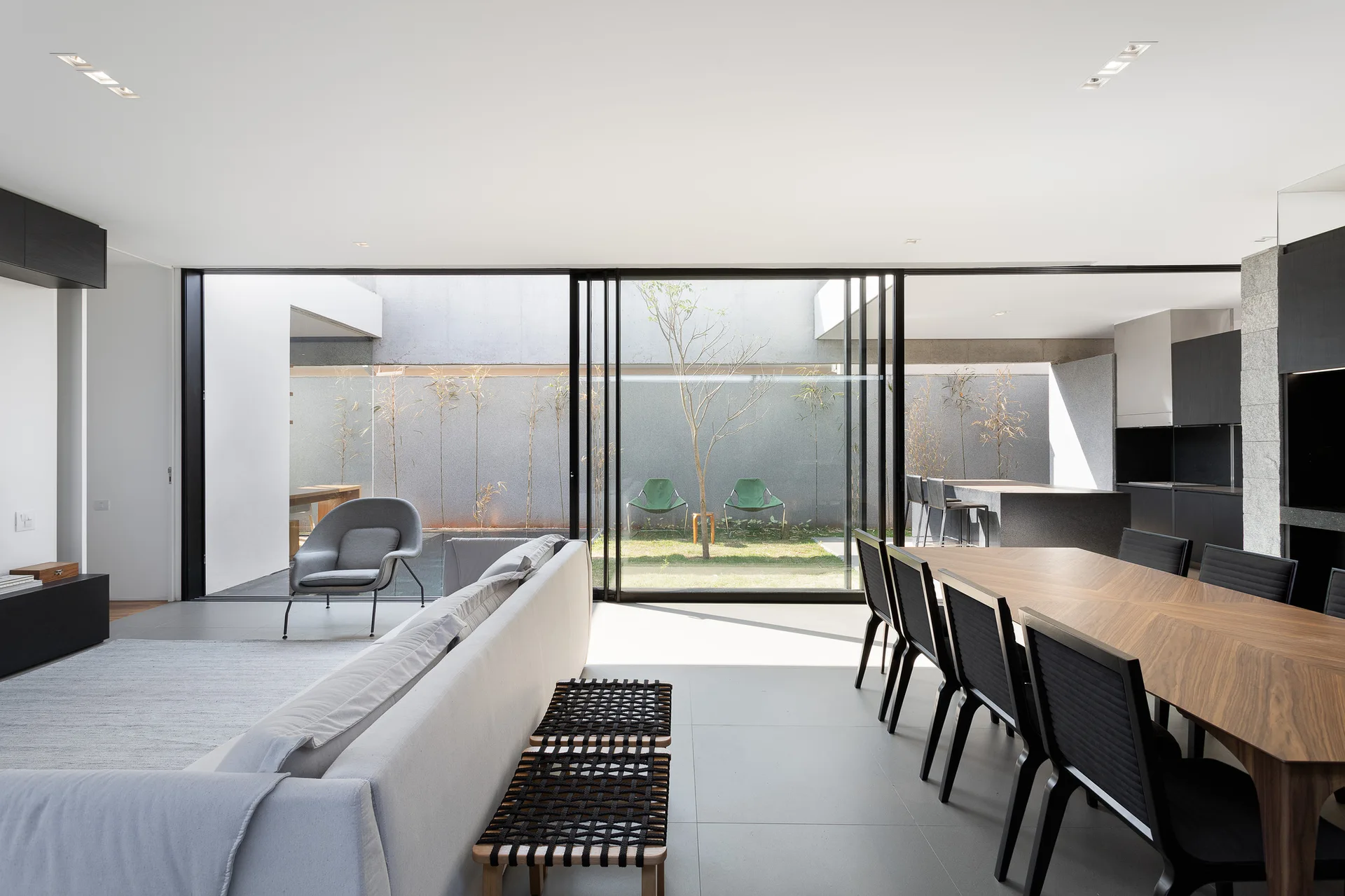 A modern open-plan living and dining area with a grey sofa, wood dining table, and large sliding glass doors opening to an outdoor courtyard.