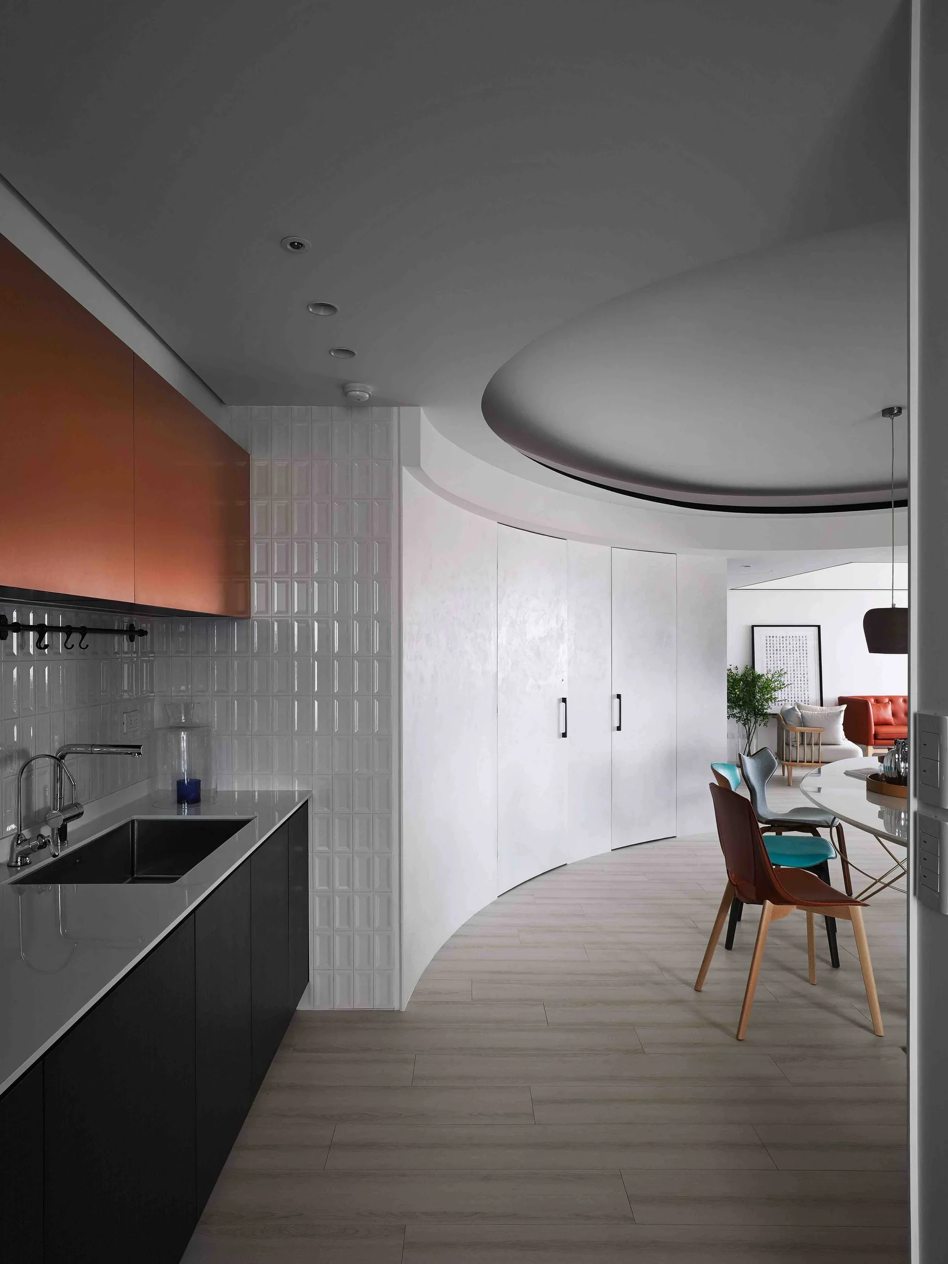 A modern kitchen featuring copper upper cabinets, a white tiled backsplash, and a curved partition wall leading to a dining area.